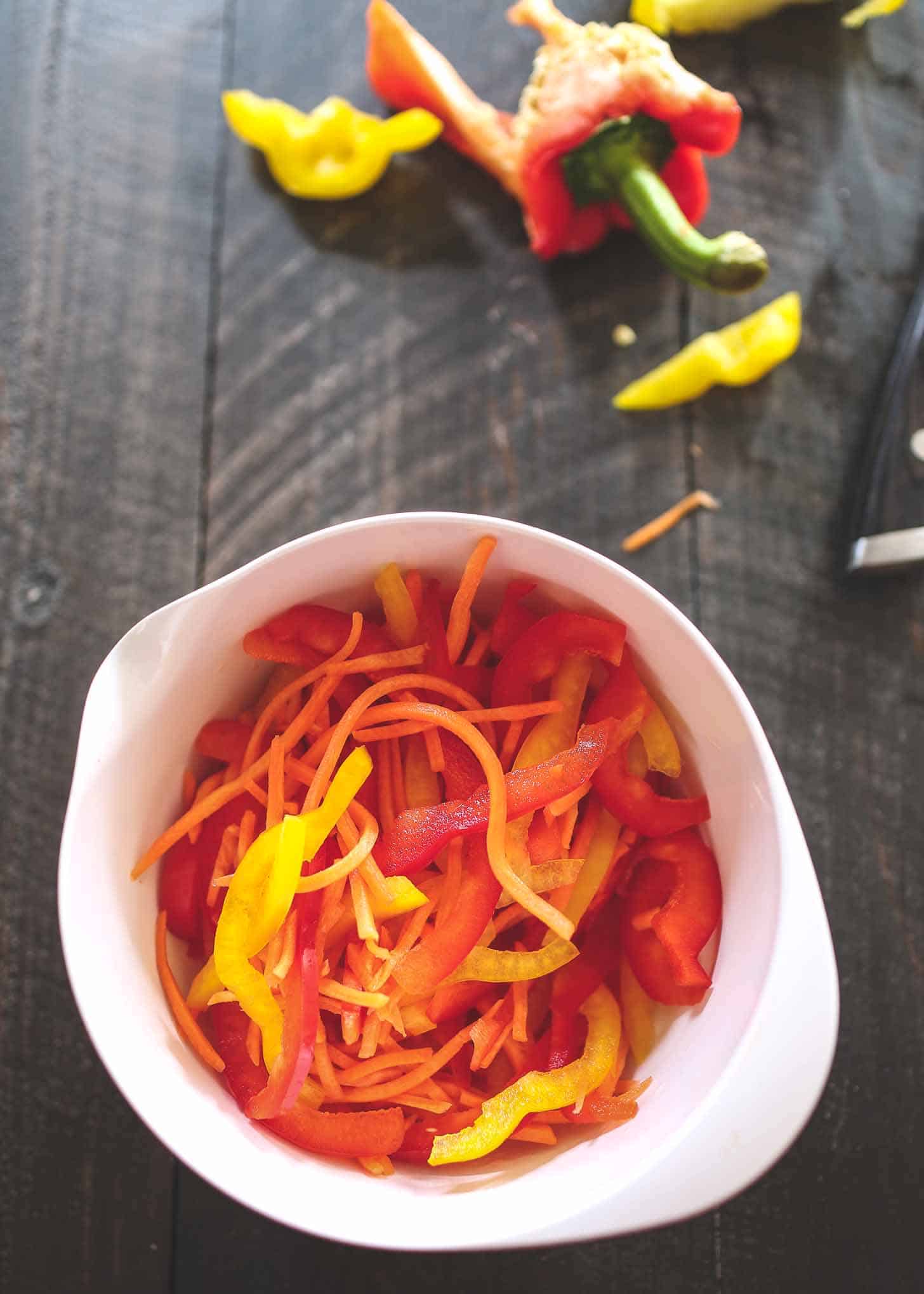 sliced red, orange and yellow bell peppers in a white bowl
