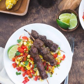 beef skewers over corn salsa on a white plate