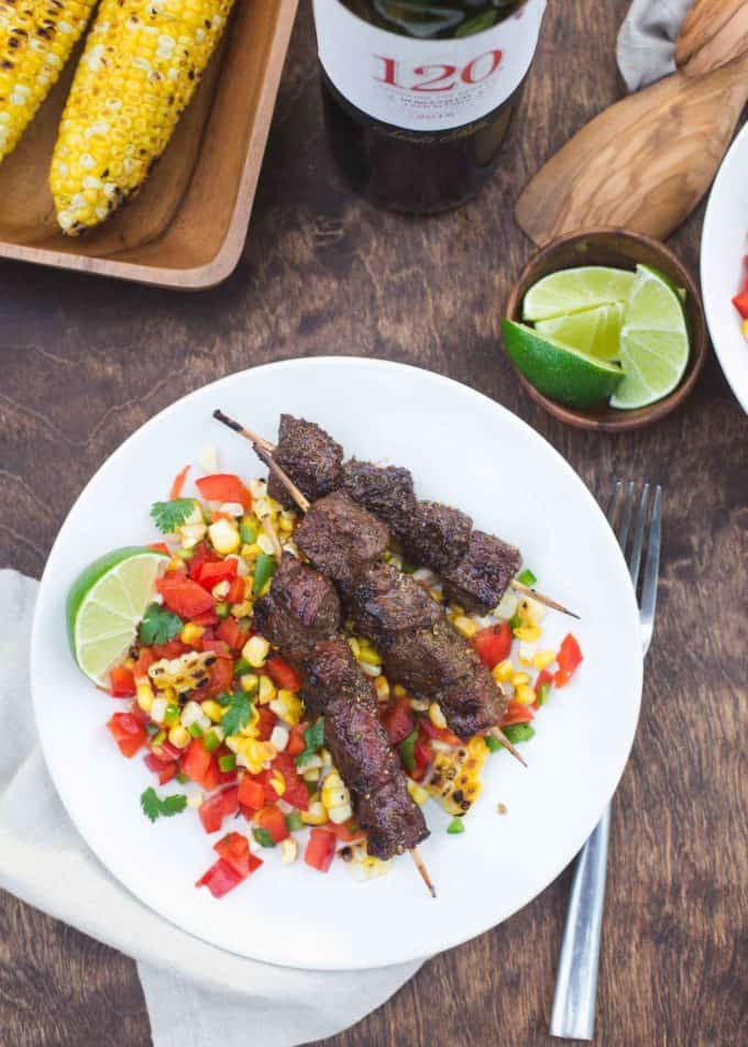 beef skewers over corn salsa on a white plate