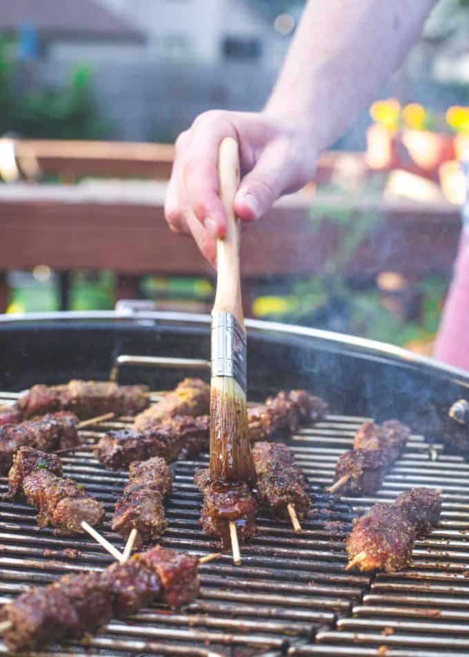 basting beef skewers on a grill