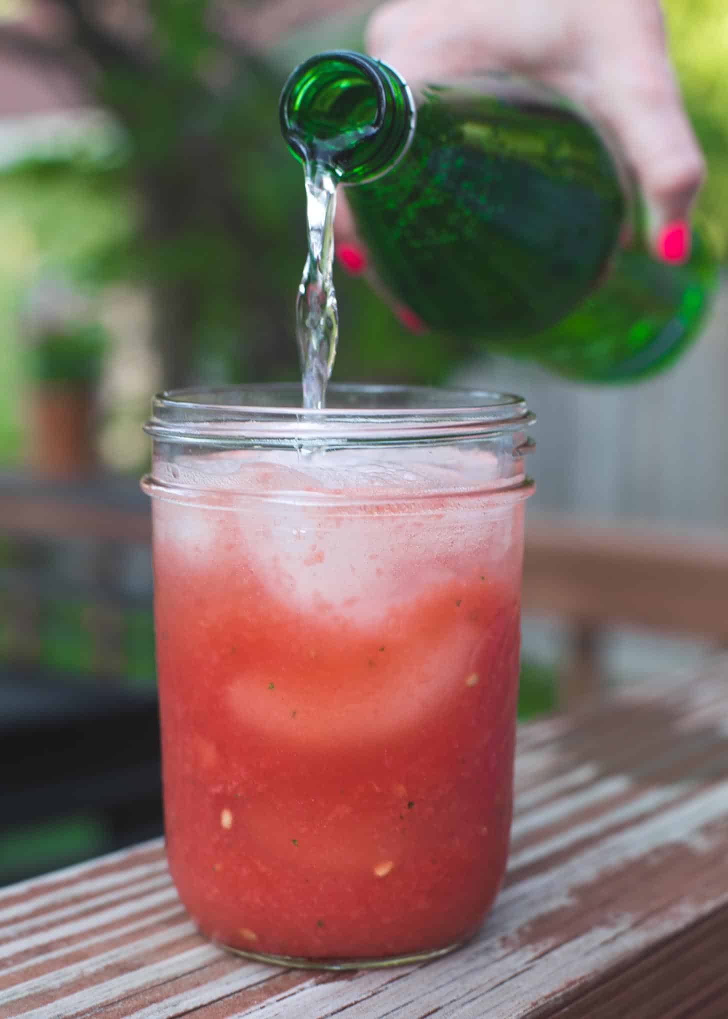 adding sparkling water to a drink in a glass jar