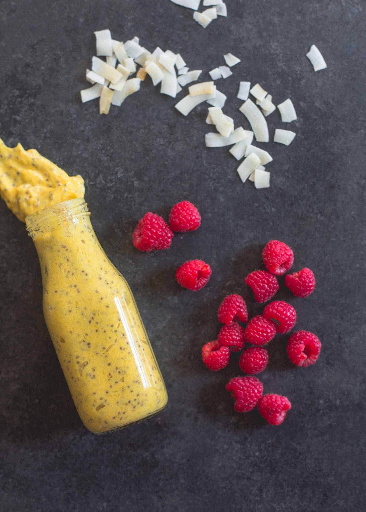 overhead image of Mango Chia mix, raspberries, and coconut flakes on a grey countertop