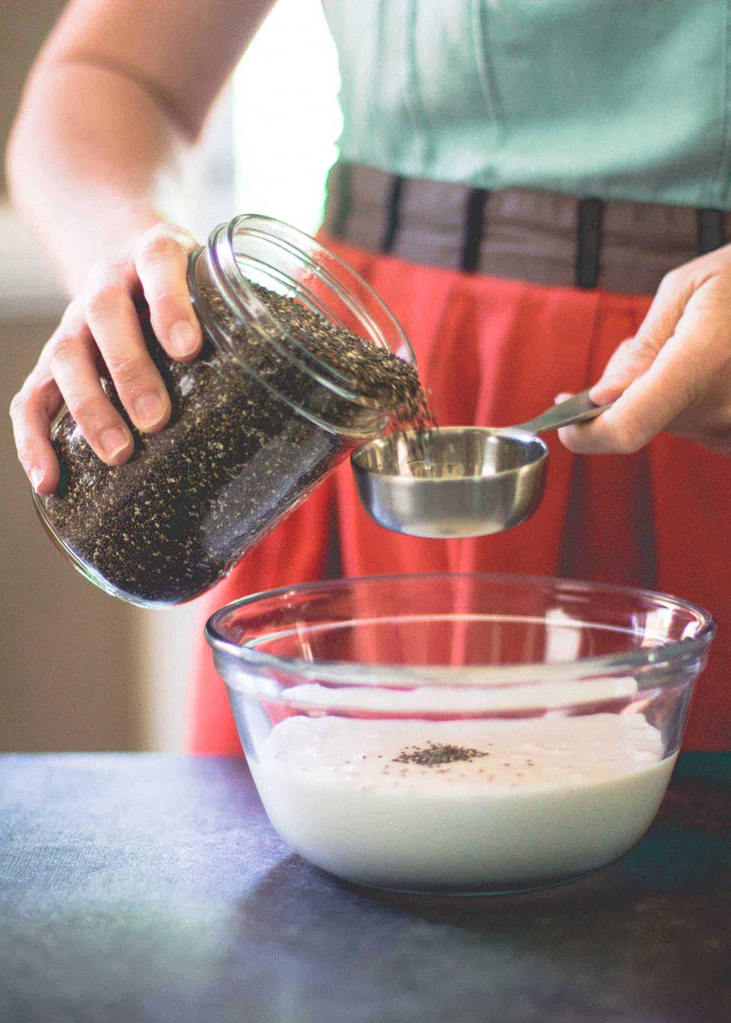 adding chia seeds to milk in a glass bowl