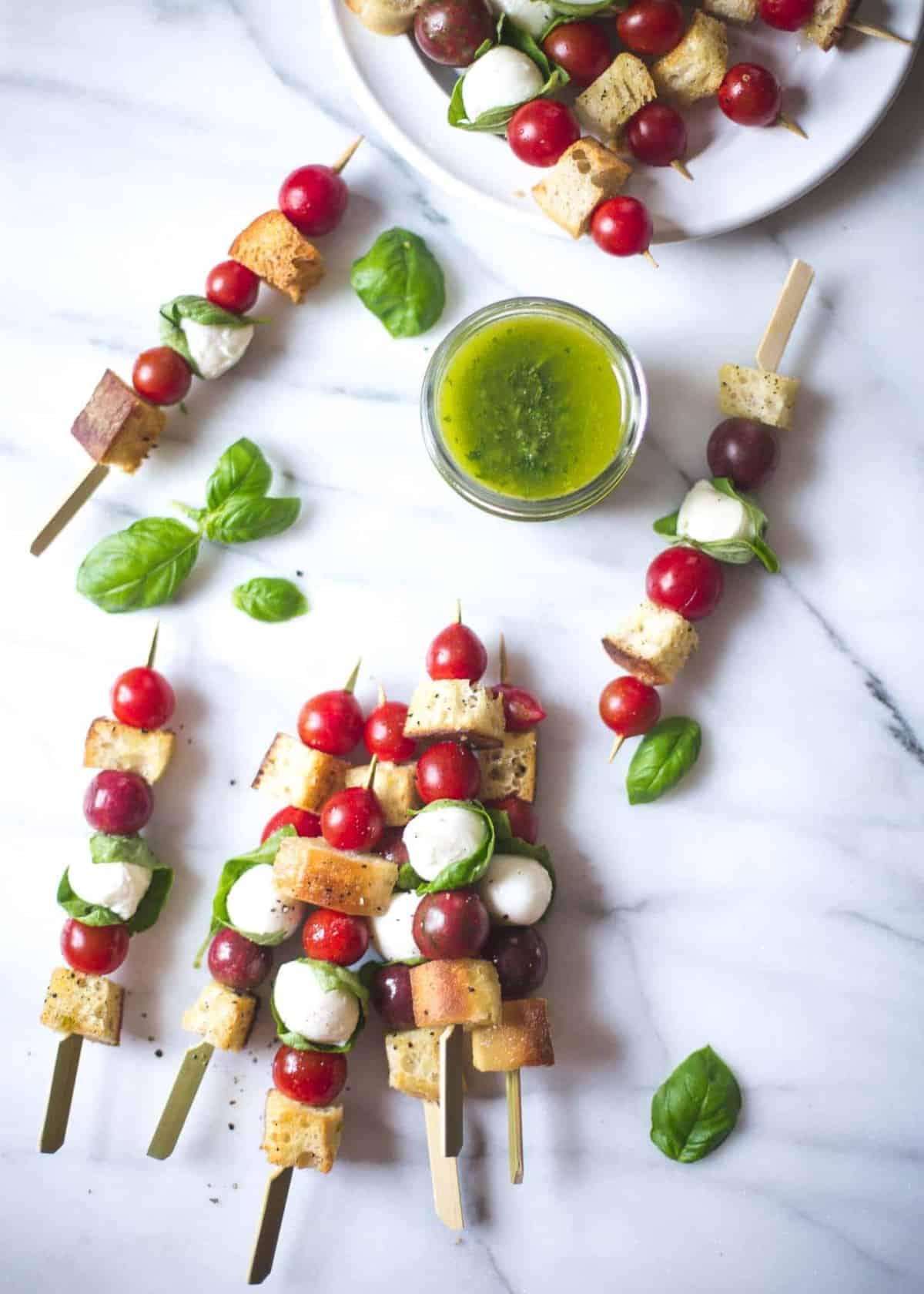 Panzanella Salad Skewers on a white table with basil leaves