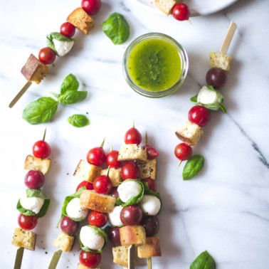 Panzanella Salad Skewers on a white table with basil leaves