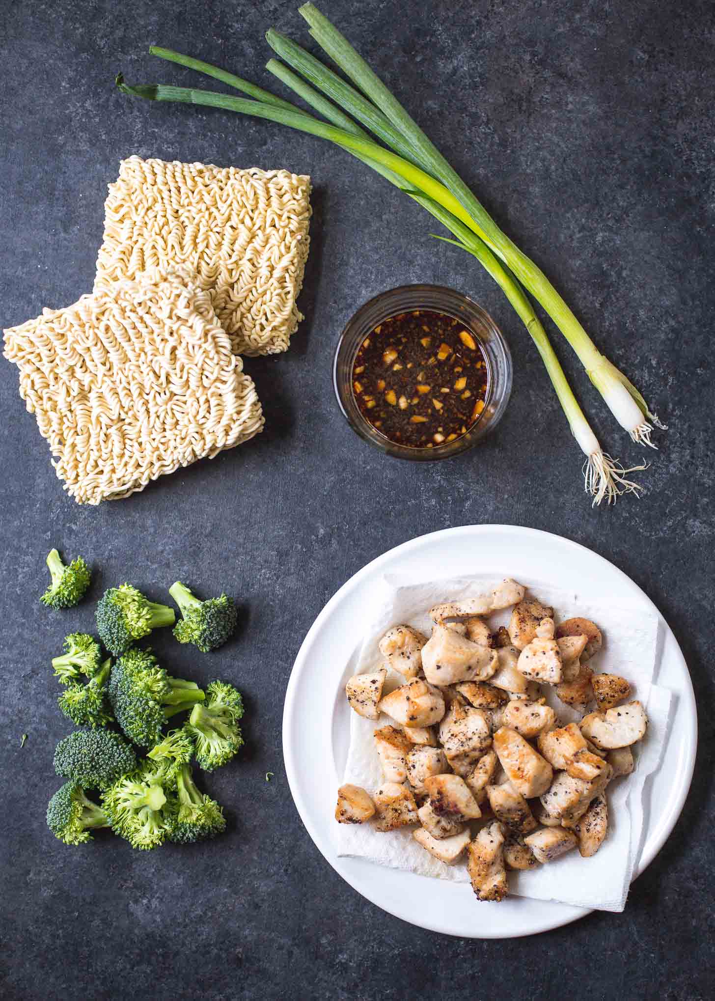 chicken, ramen, broccoli, green onions and sauce on a grey countertop