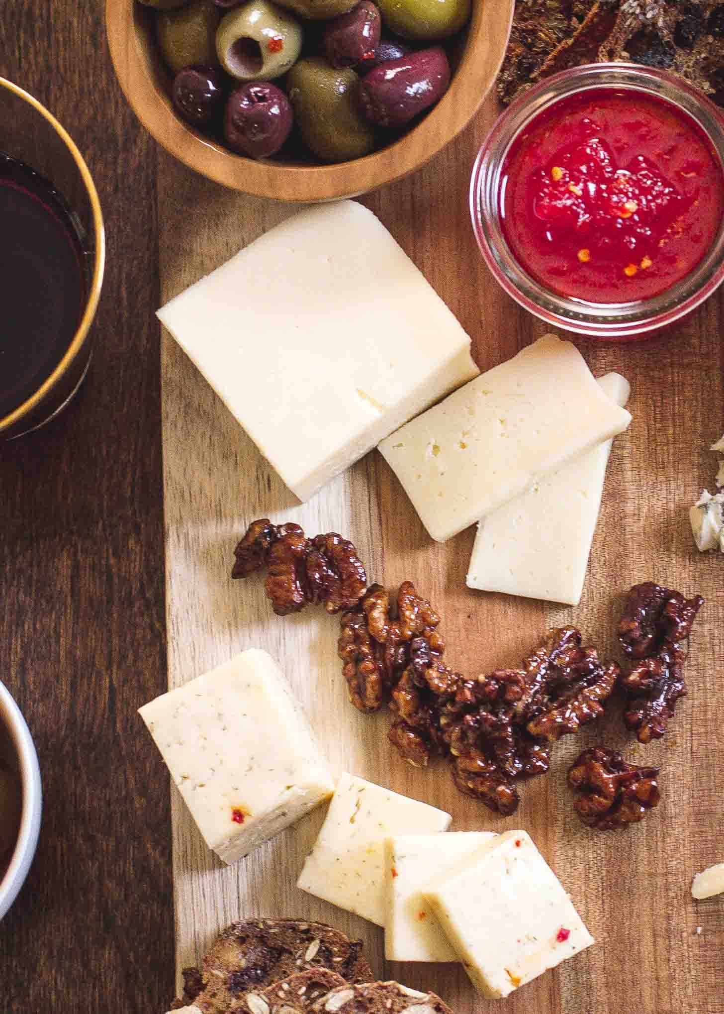 cheese, nuts, olives and red pepper jelly on a wooden tray