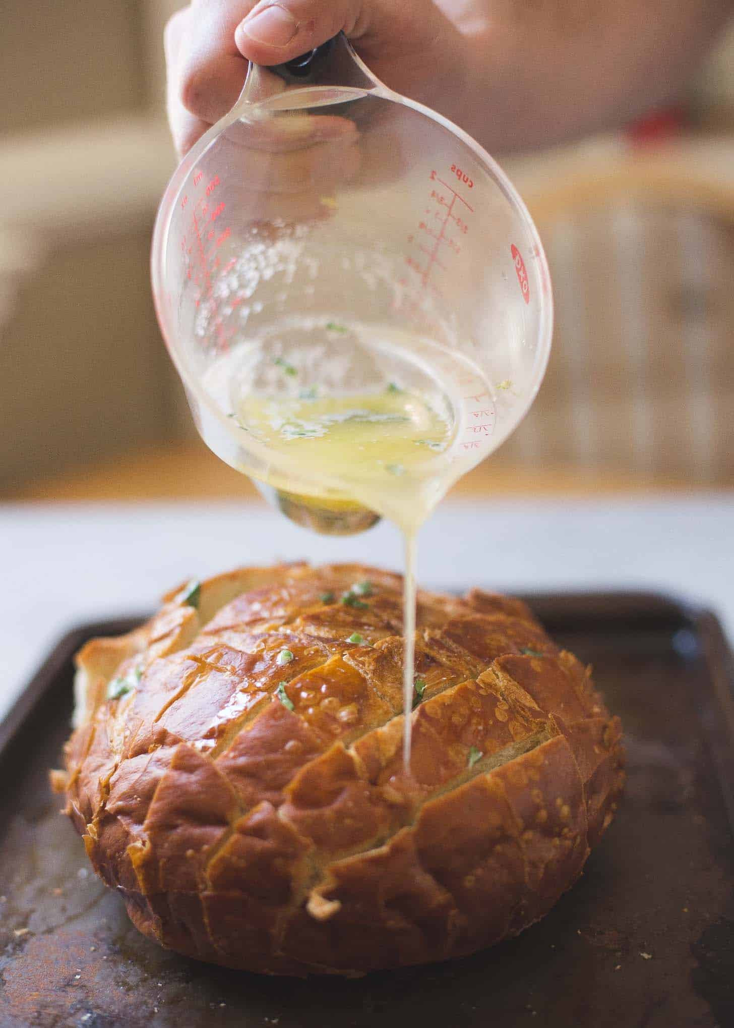 pouring garlic butter into the cuts in a round loaf of bread