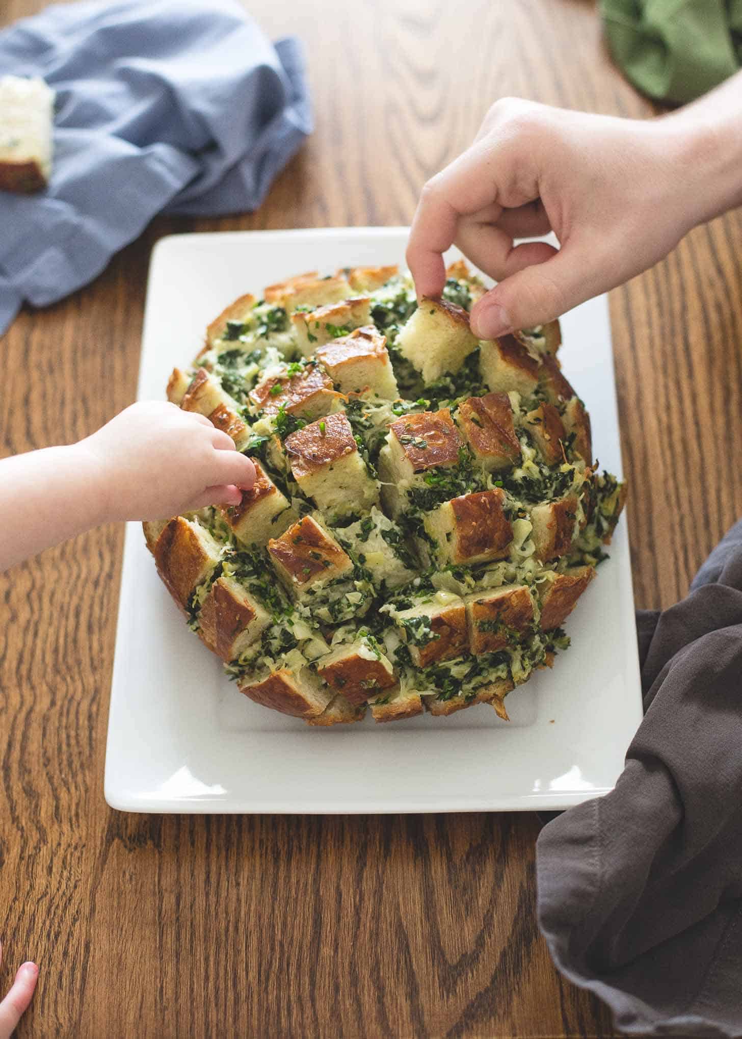 pulling pieces off the Pull Apart Bread on a white rectangular tray