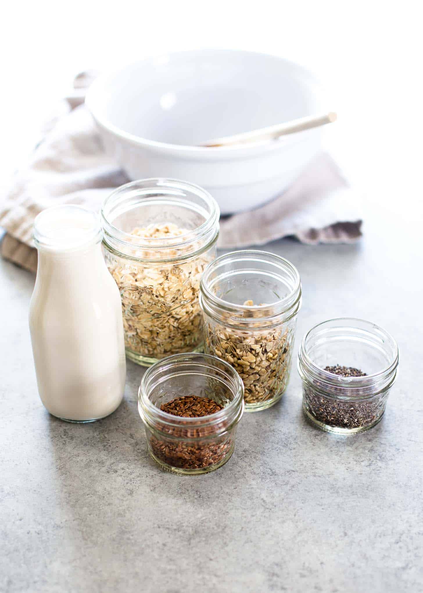 oats, chia seeds, milk and seasoning in jars on a grey countertop