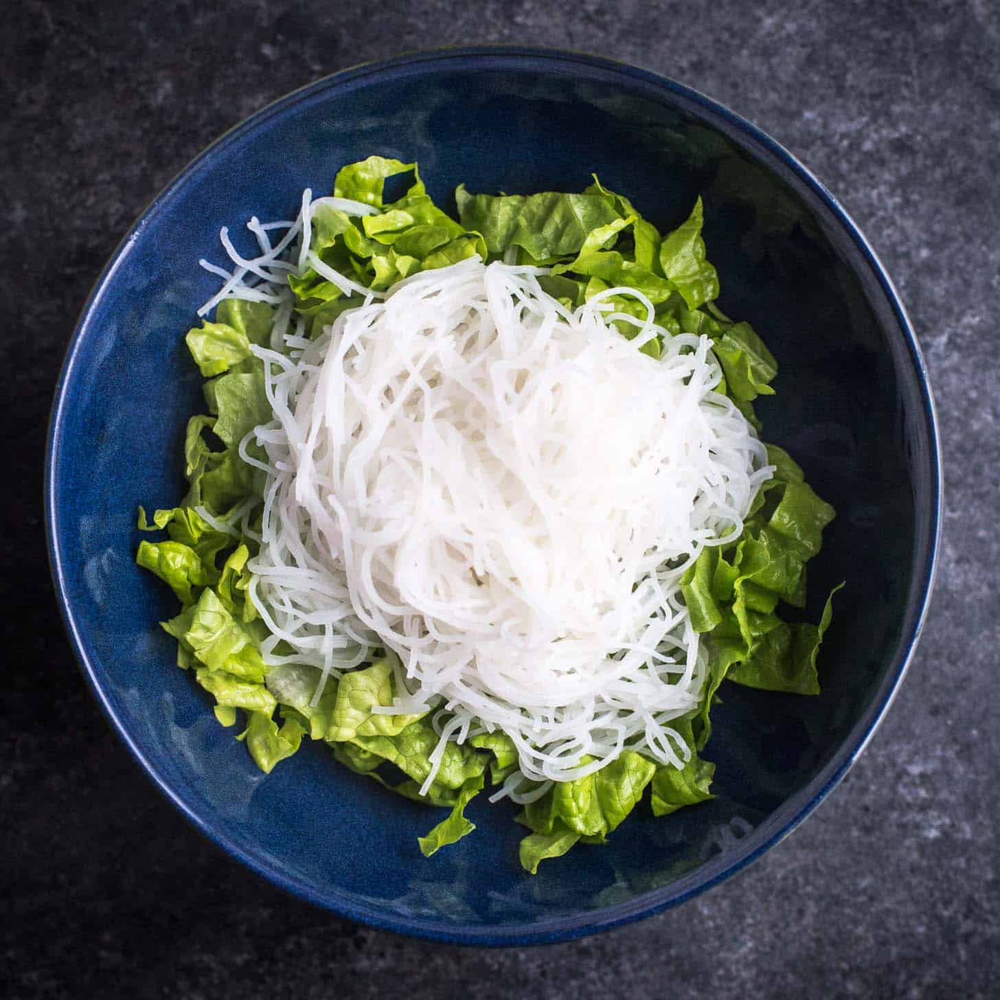 overhead image of lettuce topped with rice noodles in a blue bowl