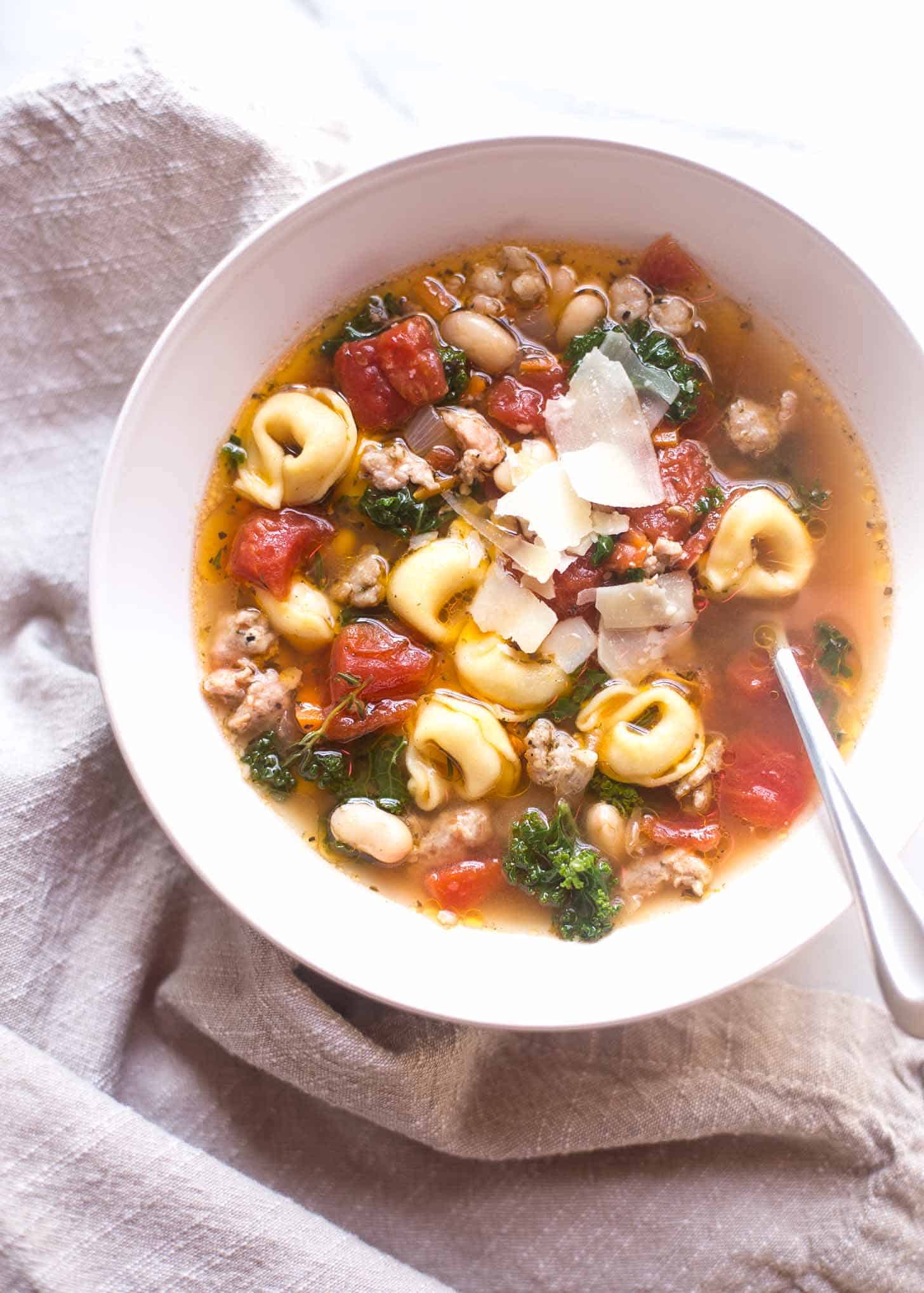 Italian Sausage Soup with Tortellini and Kale in a white bowl