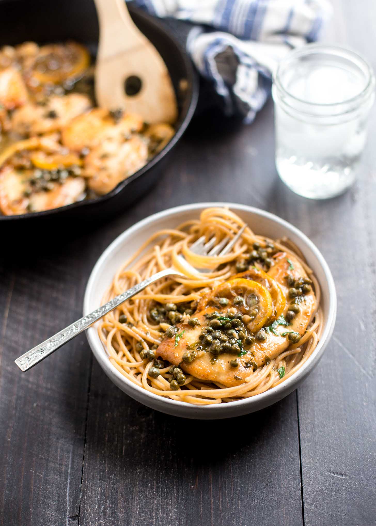 Lemon Chicken Piccata over pasta in a white bowl