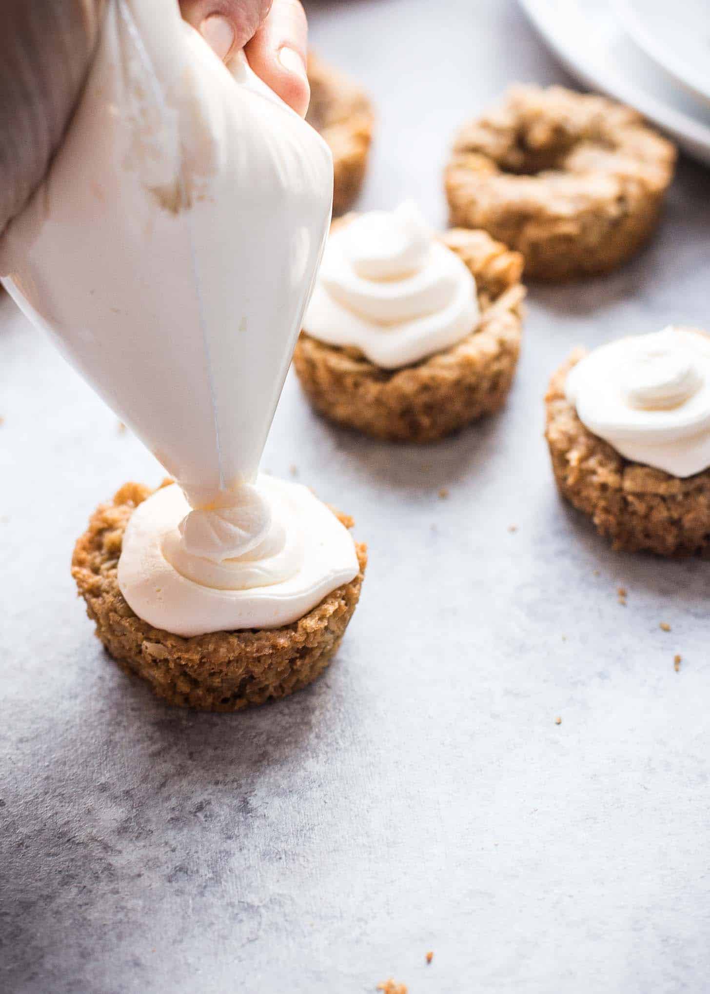 using a piping bag to pipe cream cheese icing on top of cookie cups