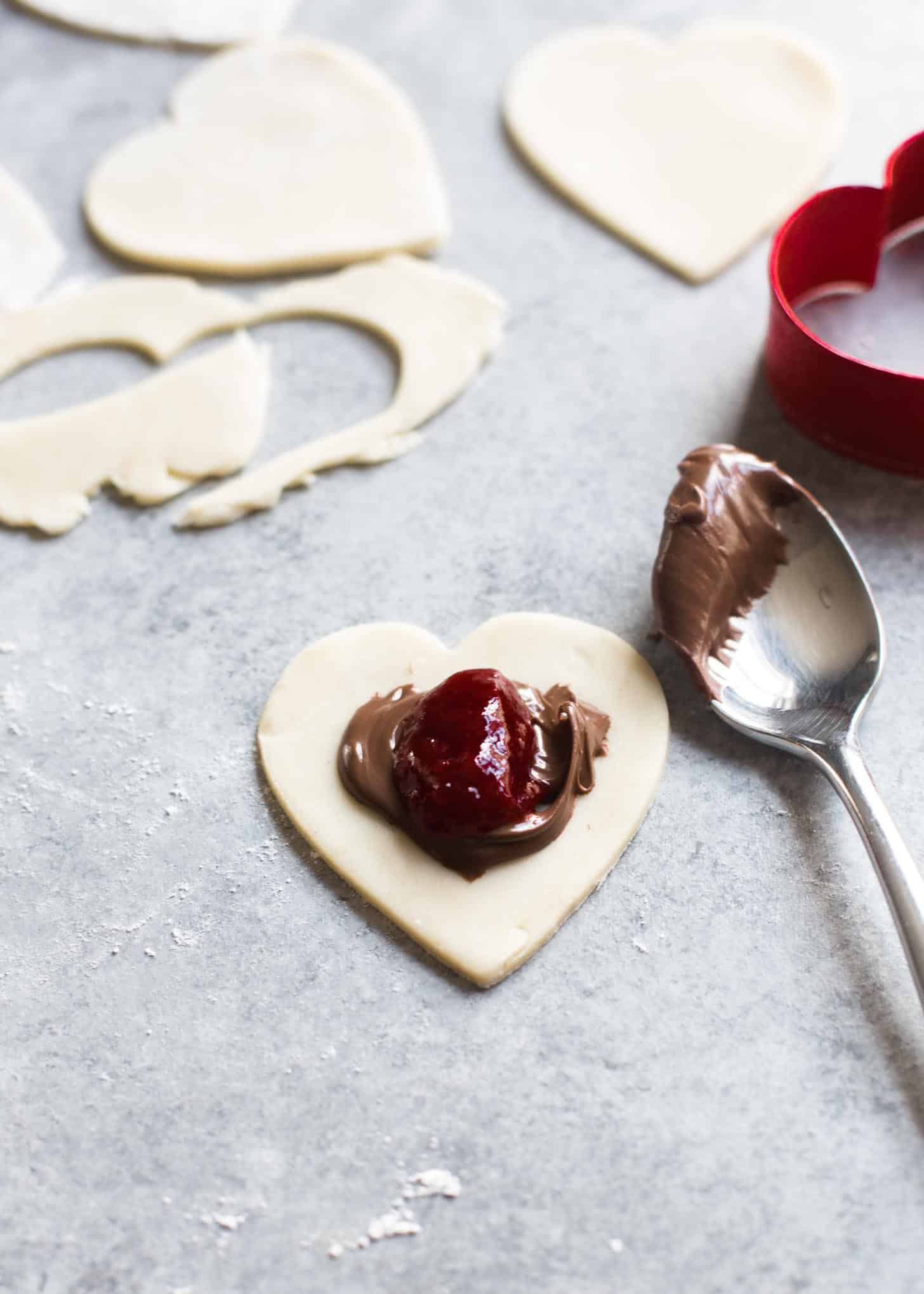 adding strawberry jam and nutella to a heart shaped piece of dough