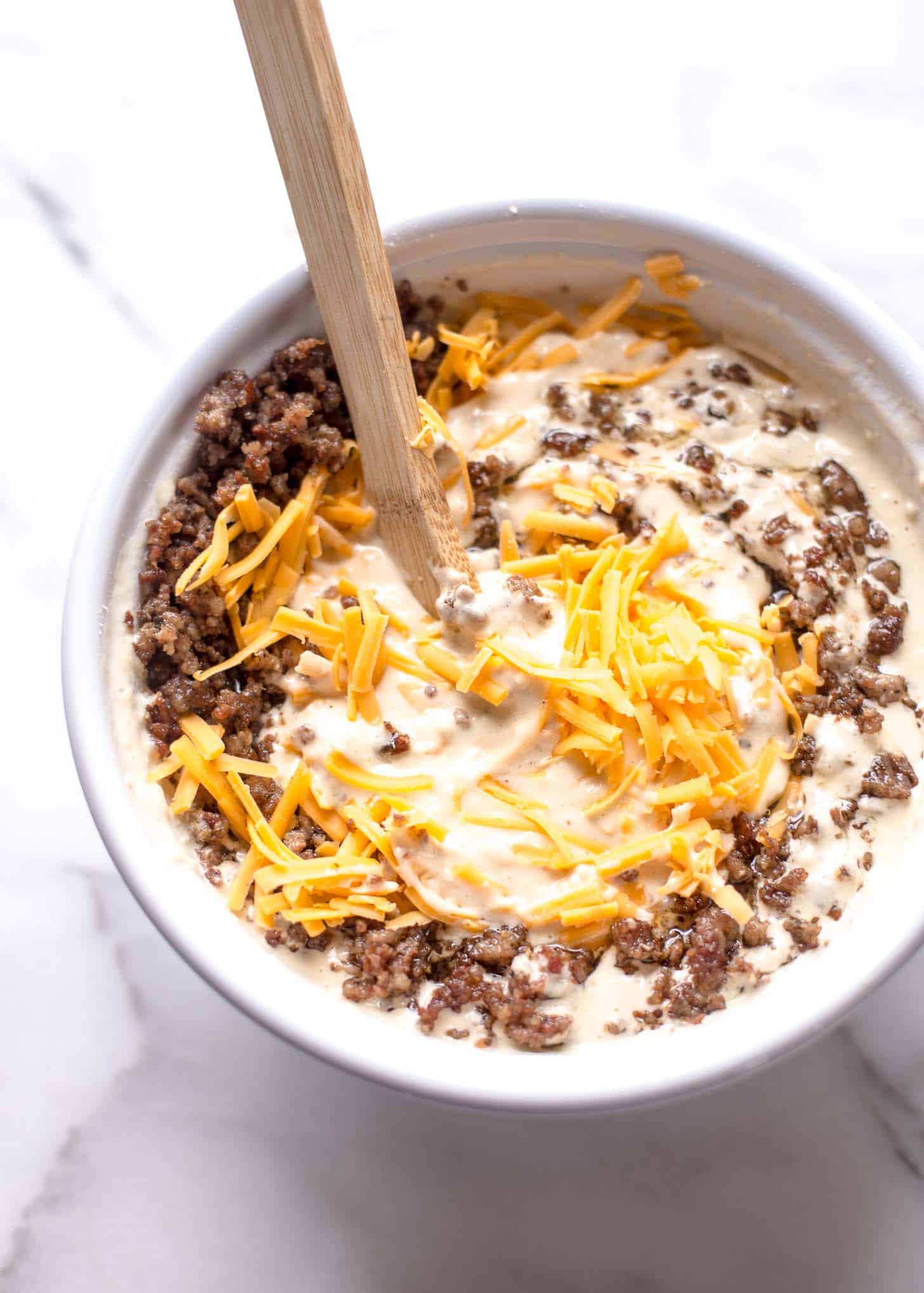 mixing cheddar and sausage with waffle mix in a white mixing bowl