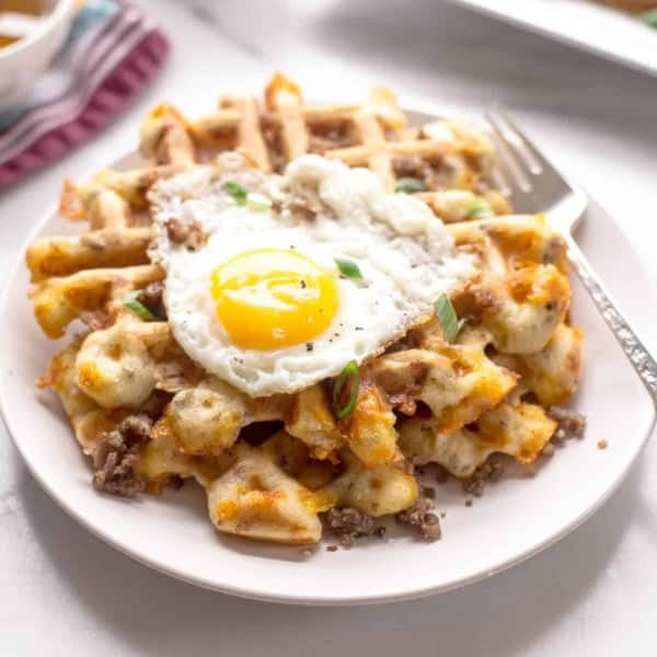 cheese and sausage savory waffles on a white plate topped with a fried egg