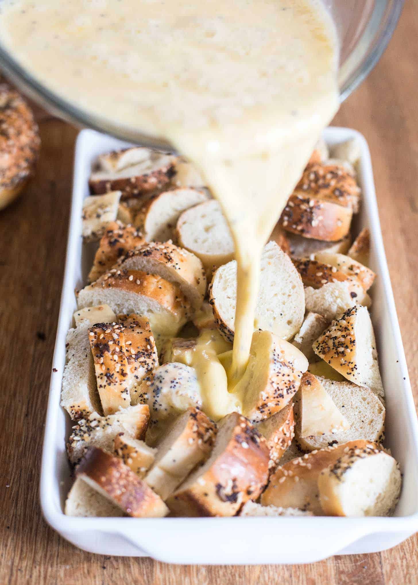 adding egg mixture to bagels in a white baking dish