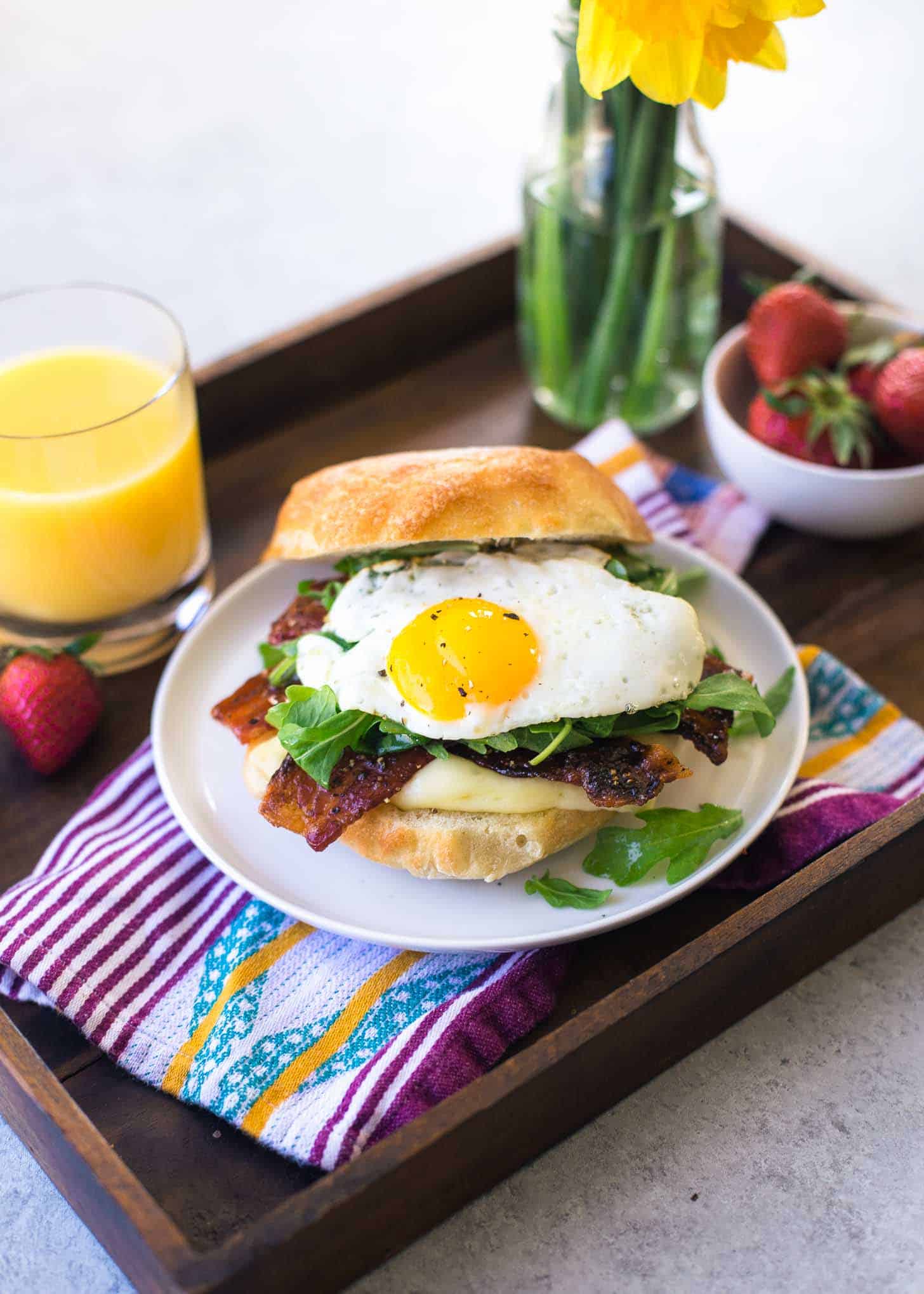 breakfast sandwich on a white plate on a wooden tray with orange juice