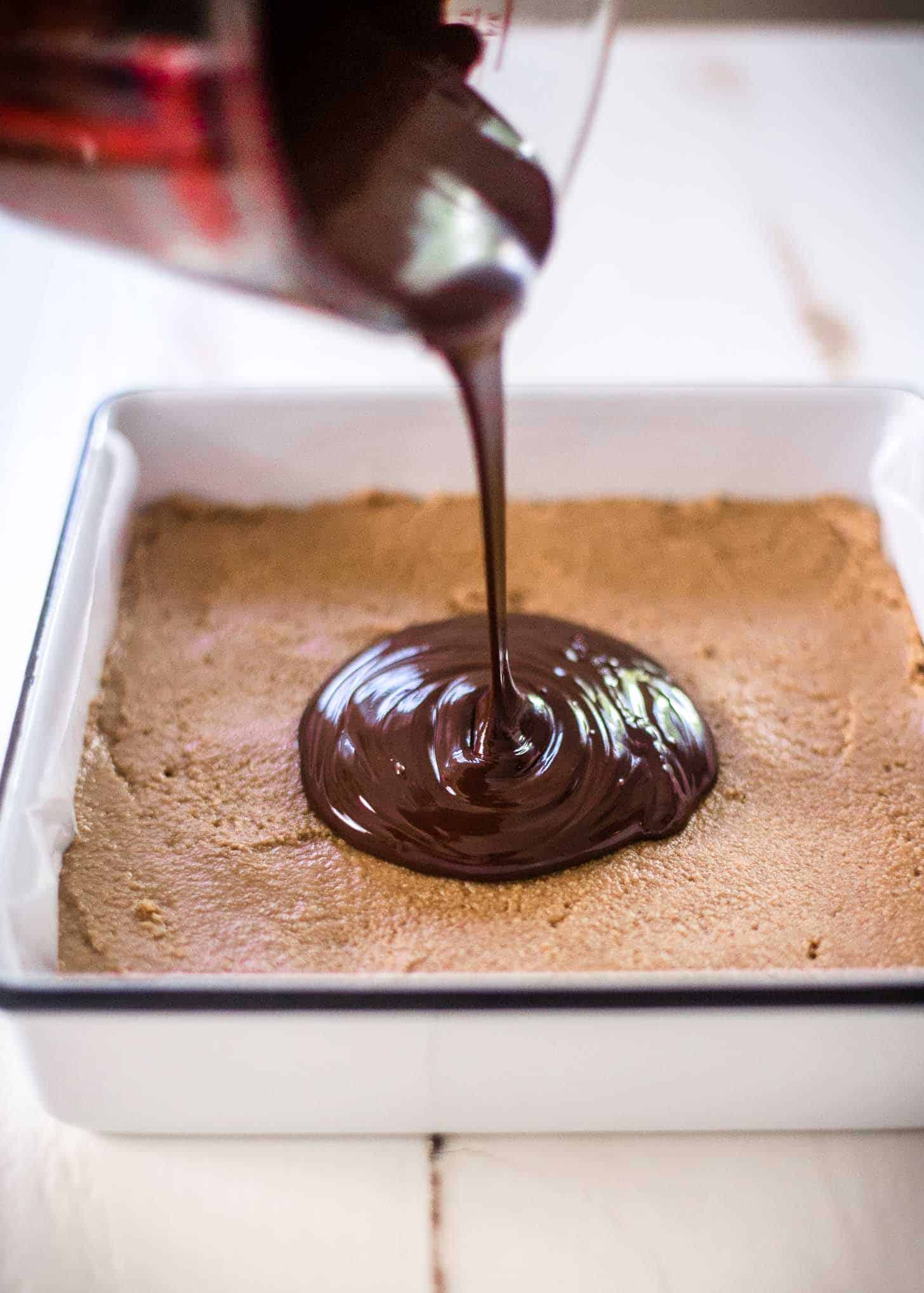 pouring chocolate over peanut butter in a white baking pan