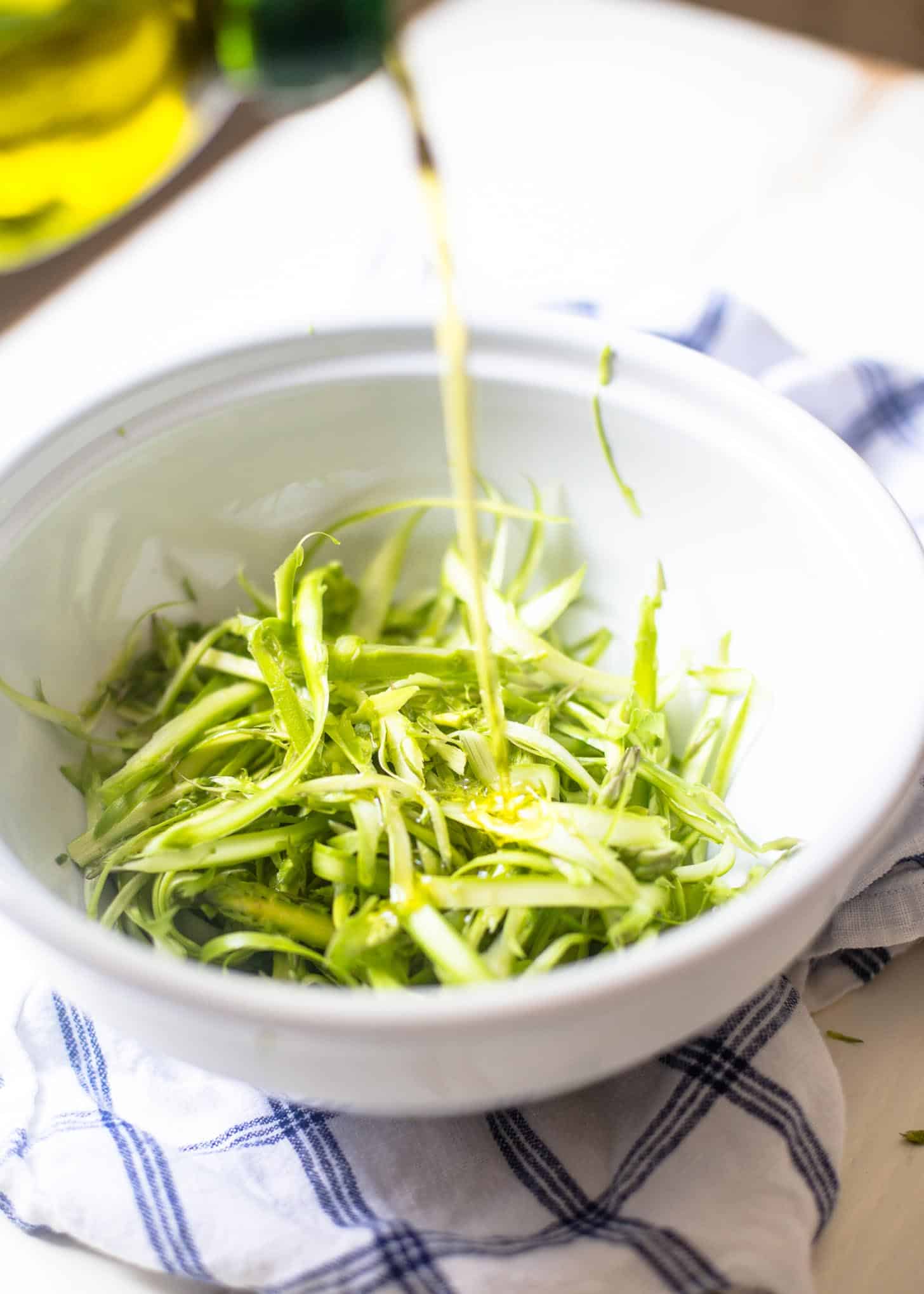 Drizzling oil on shaved asparagus in a white bowl