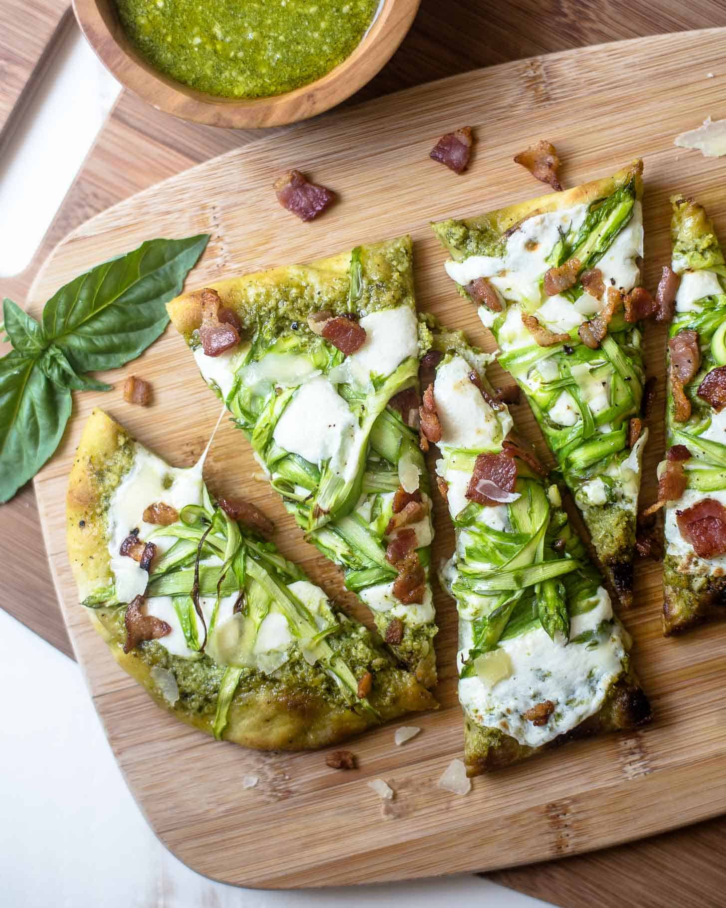 Pesto Flatbread with Shaved Asparagus and Bacon, sliced on a wooden cutting board