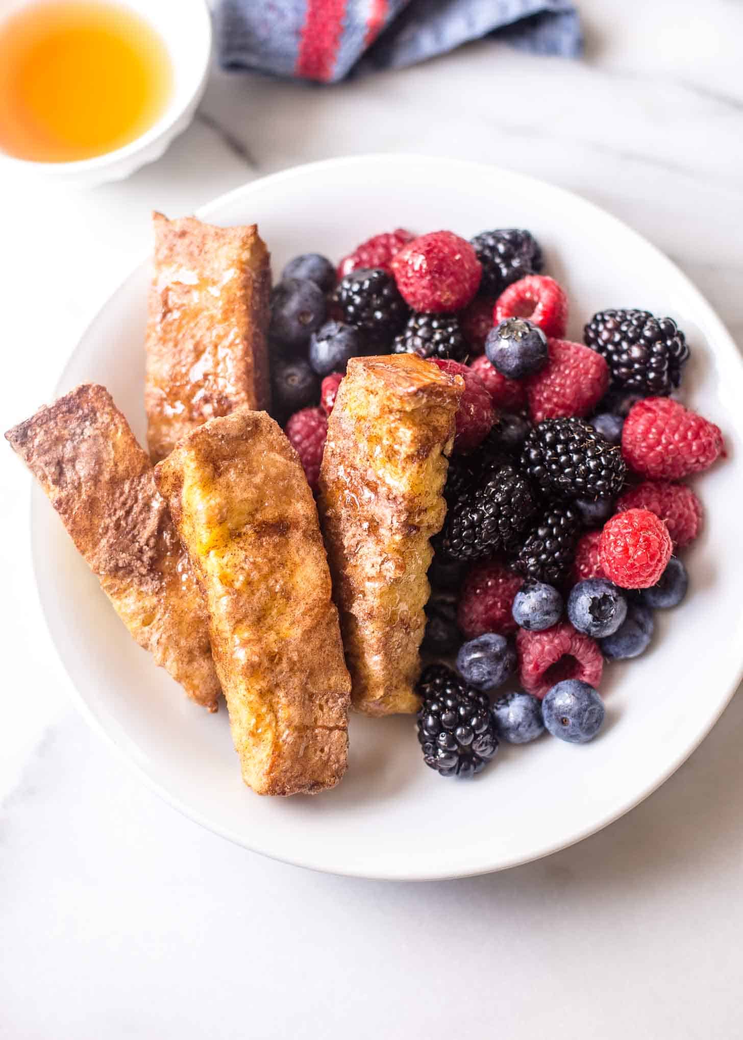 overhead image of Baked Cinnamon French Toast Sticks with berries on a white plate