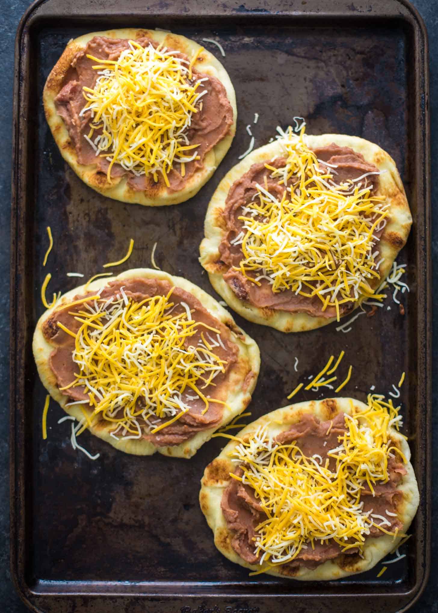 Mexican Pita Pizzas topped with cheese on a sheet pan