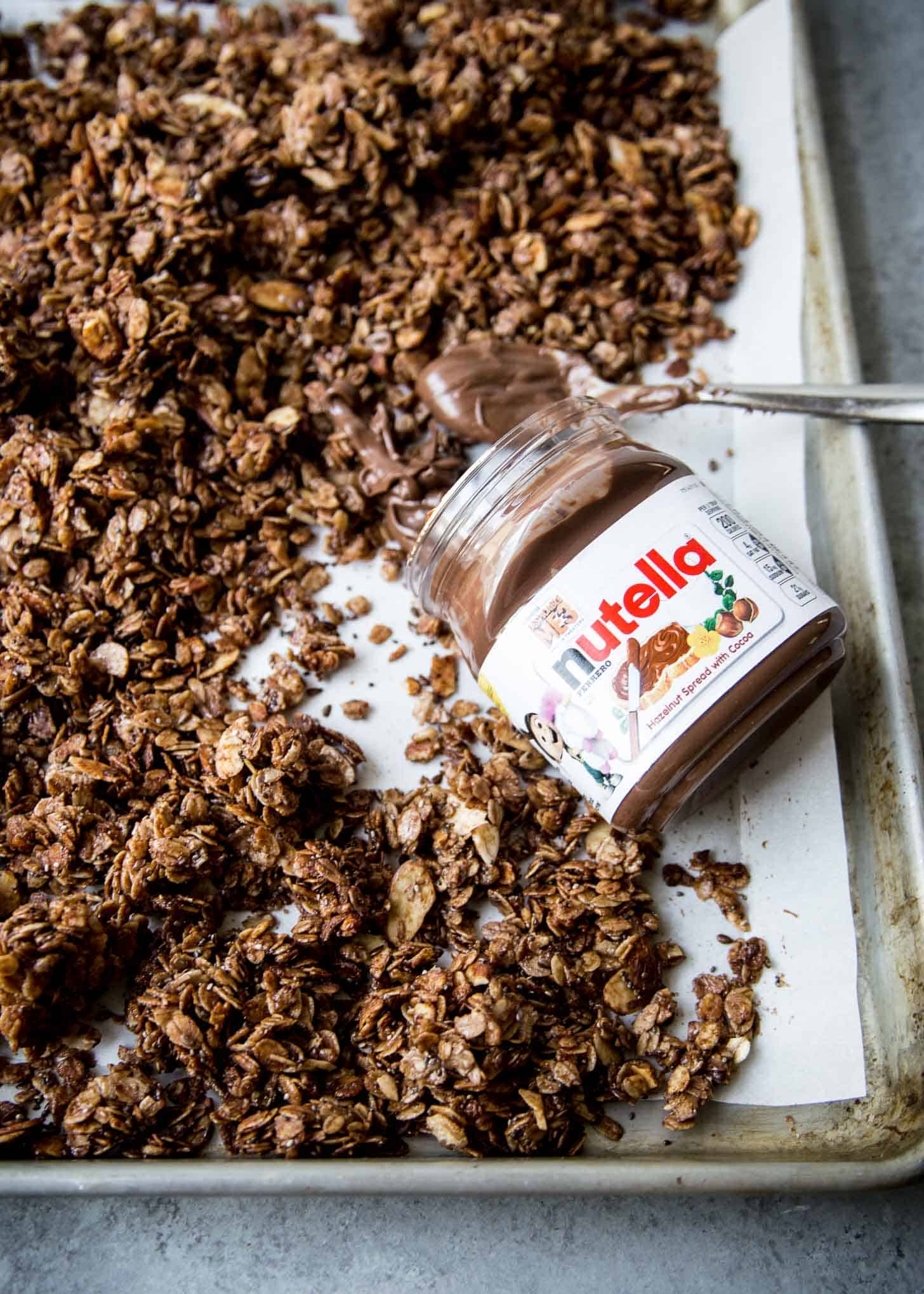 adding nutella to granola on a parchment lined sheet pan