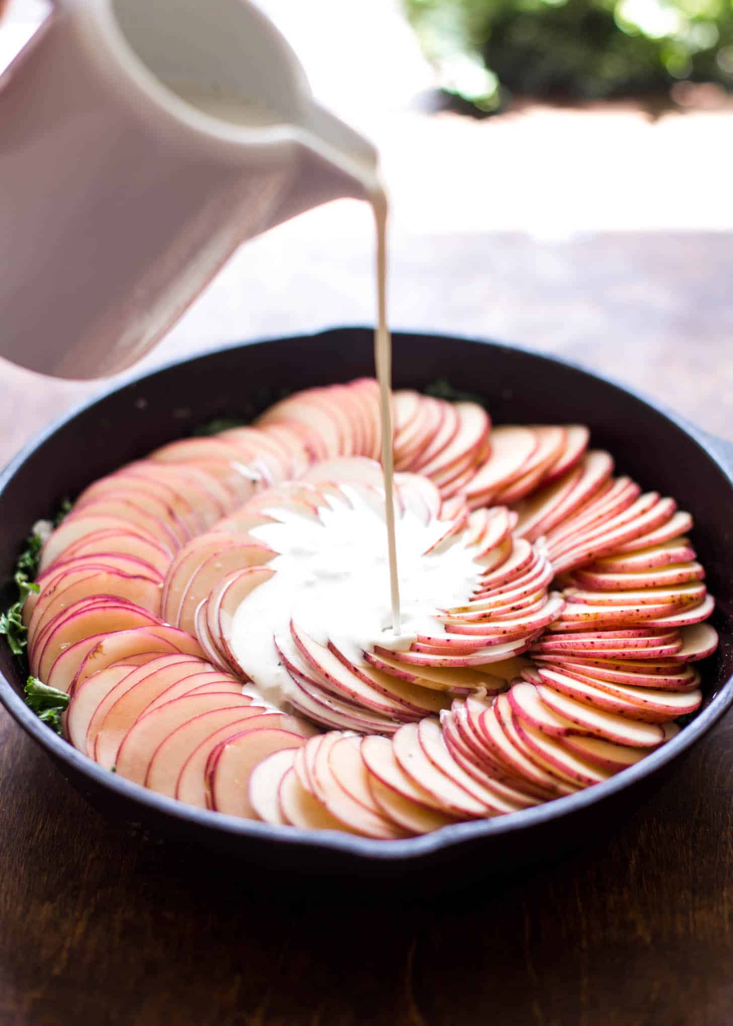 adding cream to potatoes and kale in a cast iron skillet