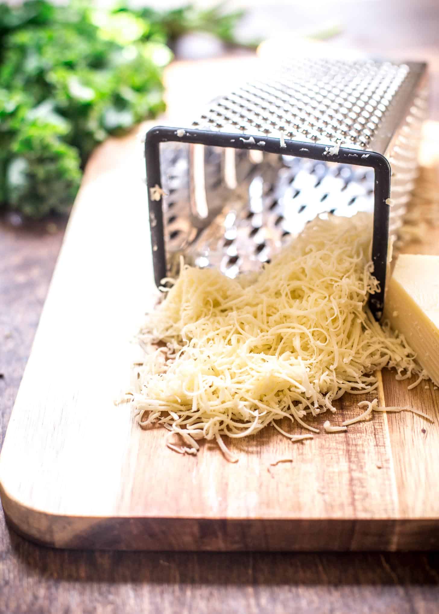 grating gruyere cheese on a wooden cutting board