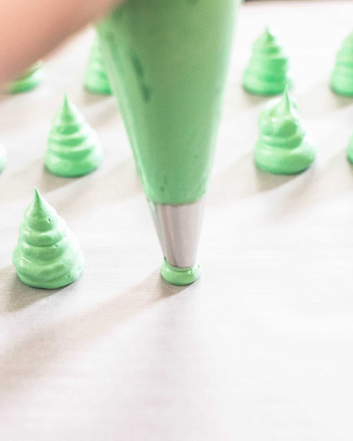 piping green meringues on a parchment lined sheet pan