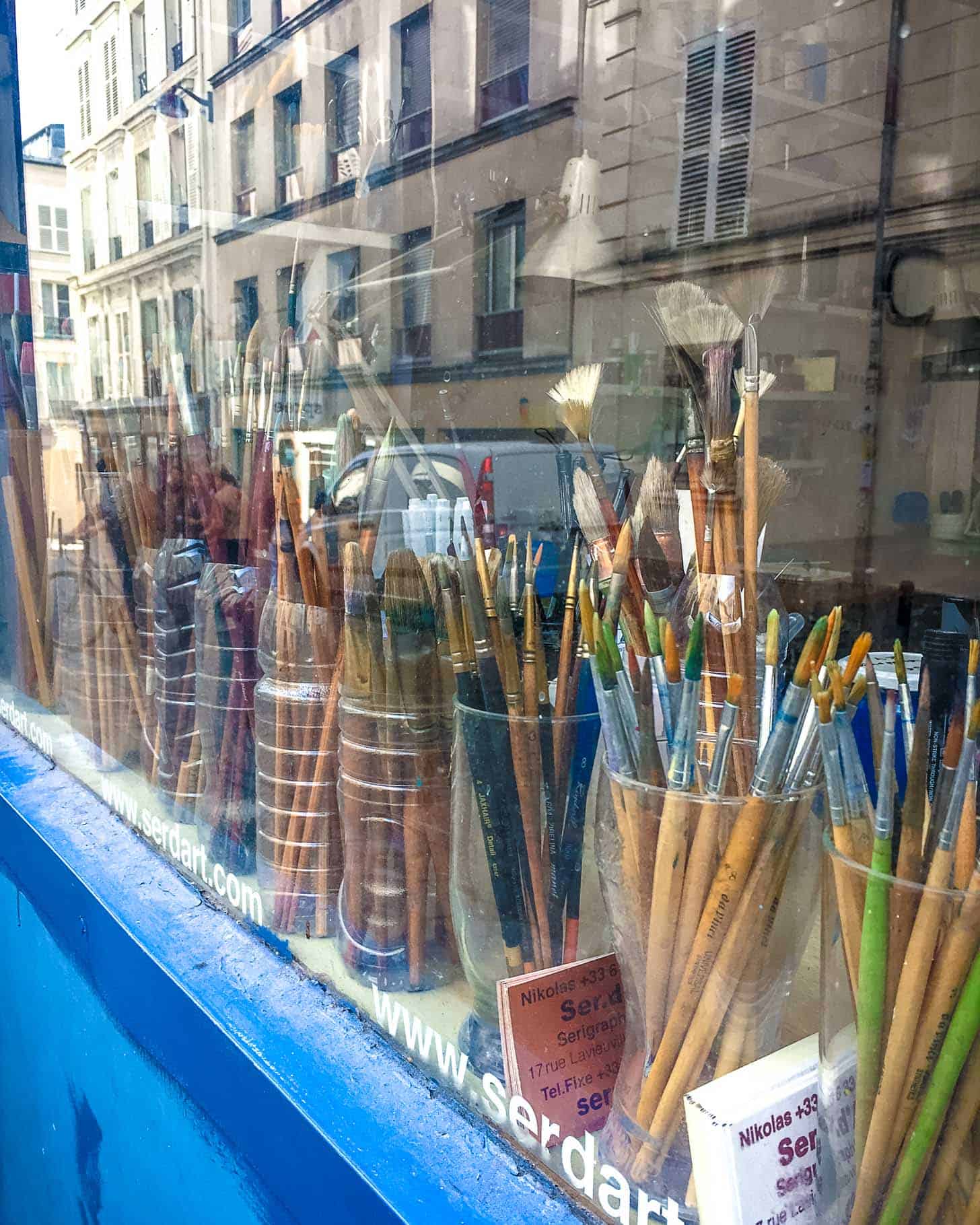 paint brushes in cups in a Paris window