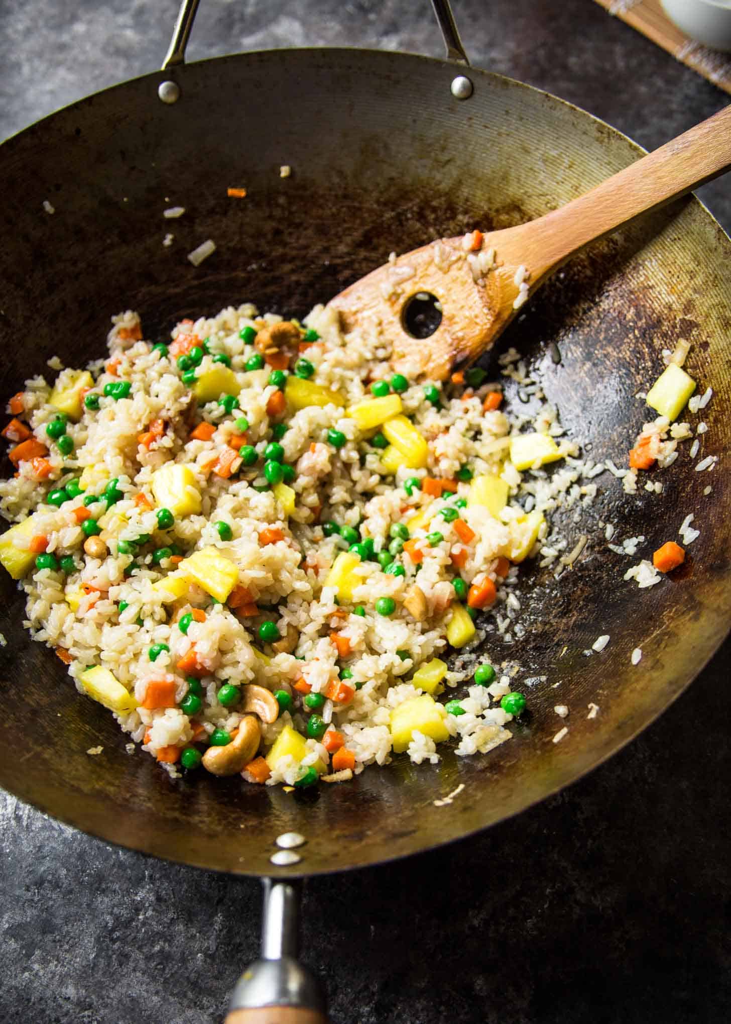 stirring fried rice in a wok with a wooden spoon