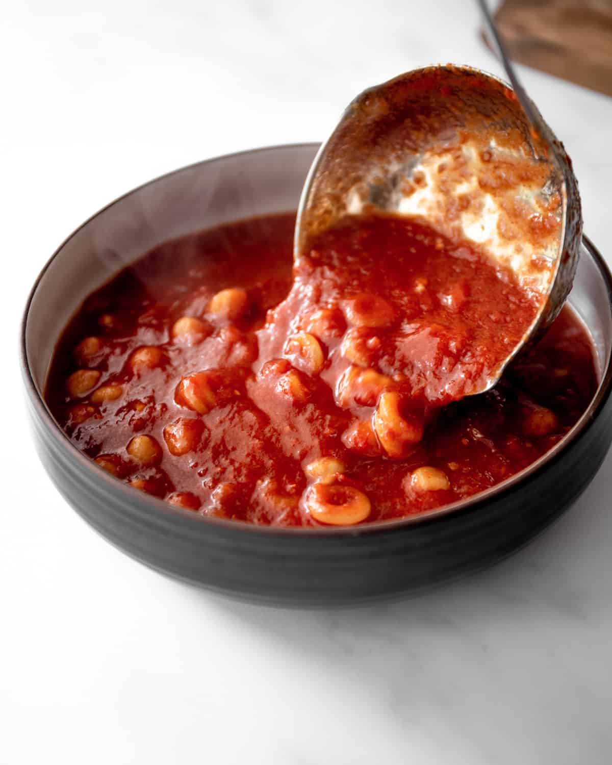 a ladle pouring tomato chickpea soup into a bowl