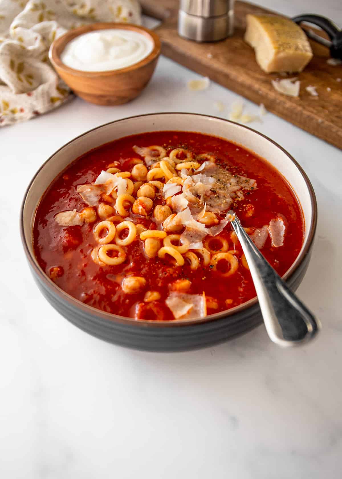 tomato soup with chickpeas and annelini pasta in tomato soup with a spoon and parmesan cheese in the background