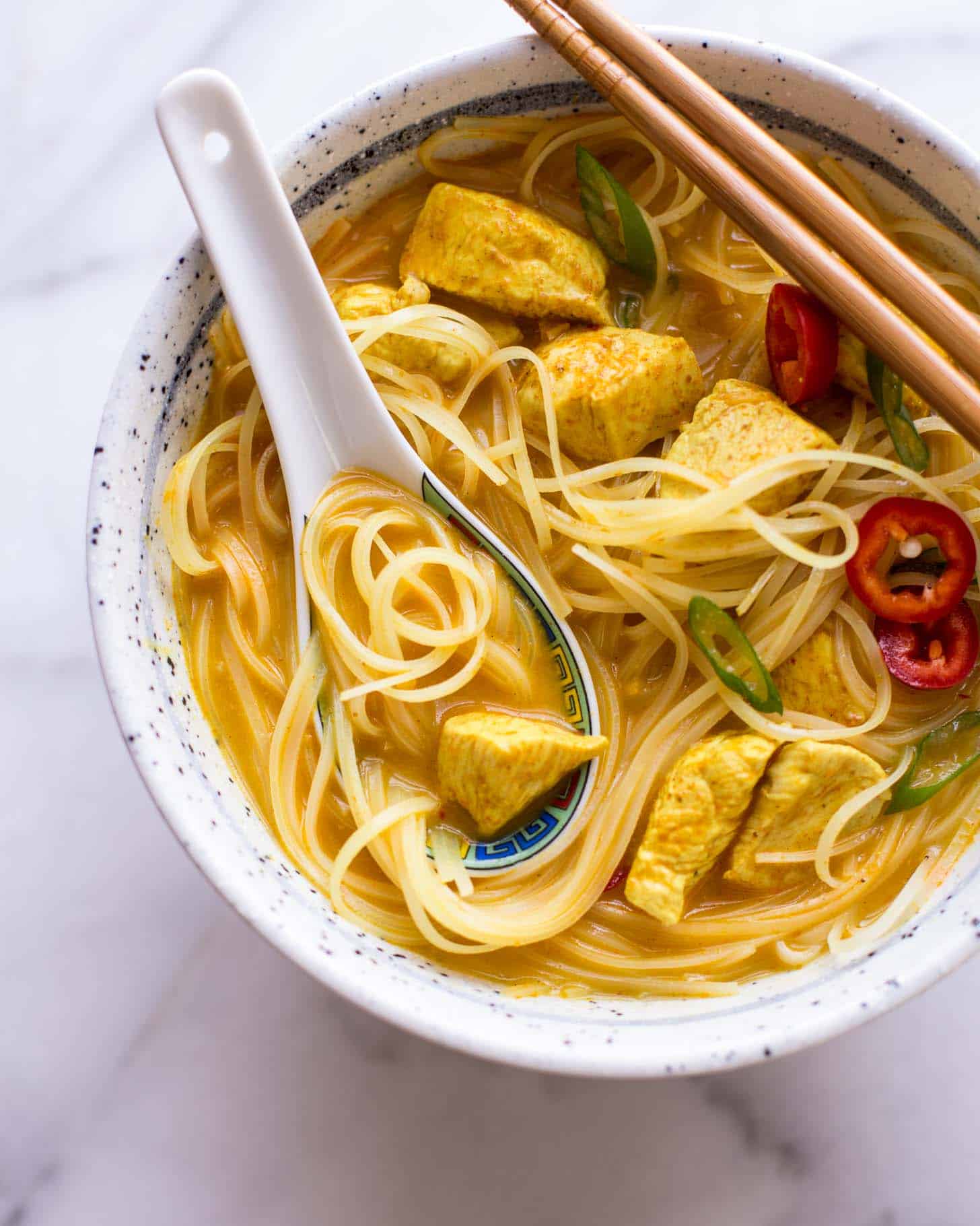 Thai Curry Noodle Soup with Chicken in a bowl with a spoon and chopsticks