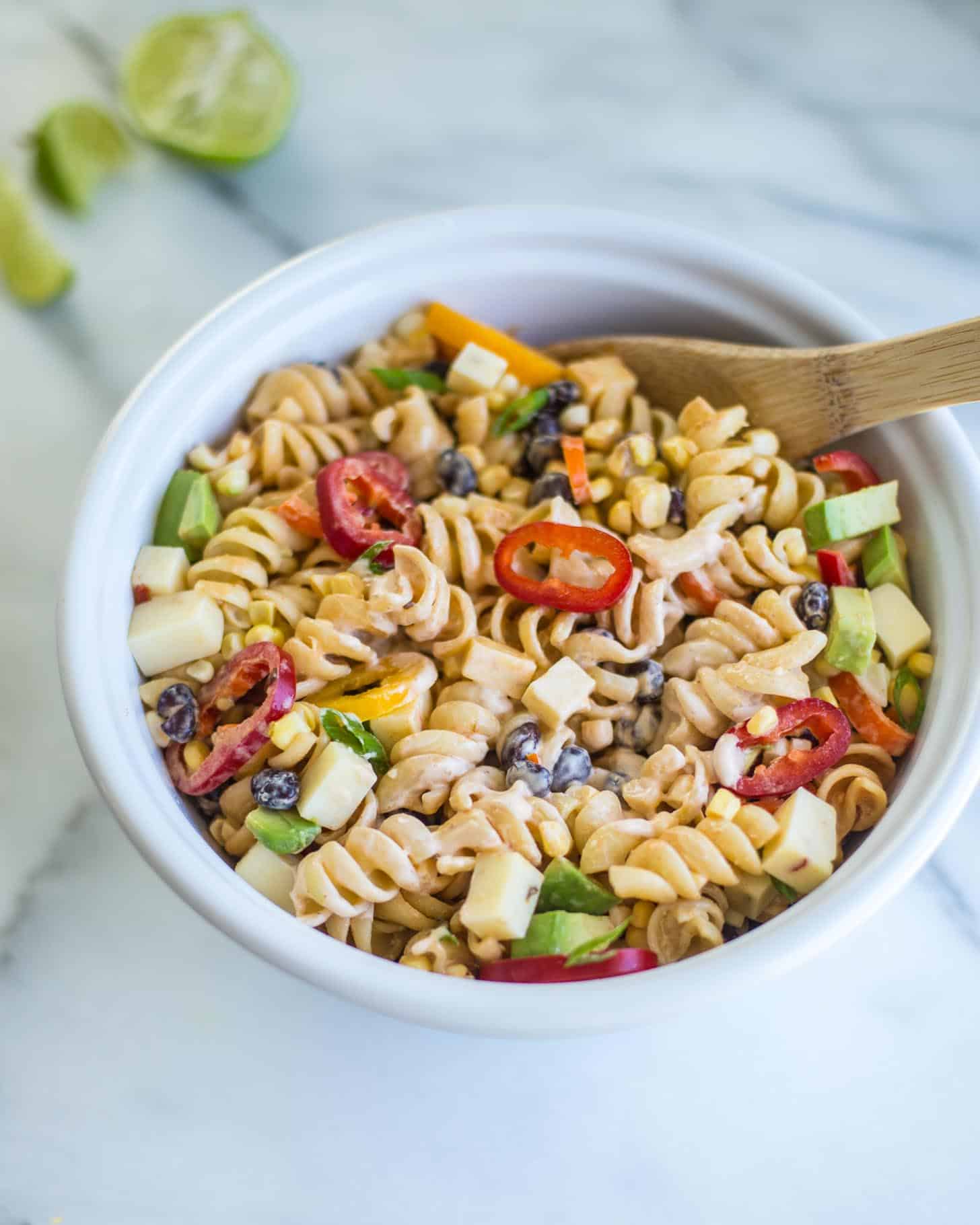 stirring pasta salad in a white bowl