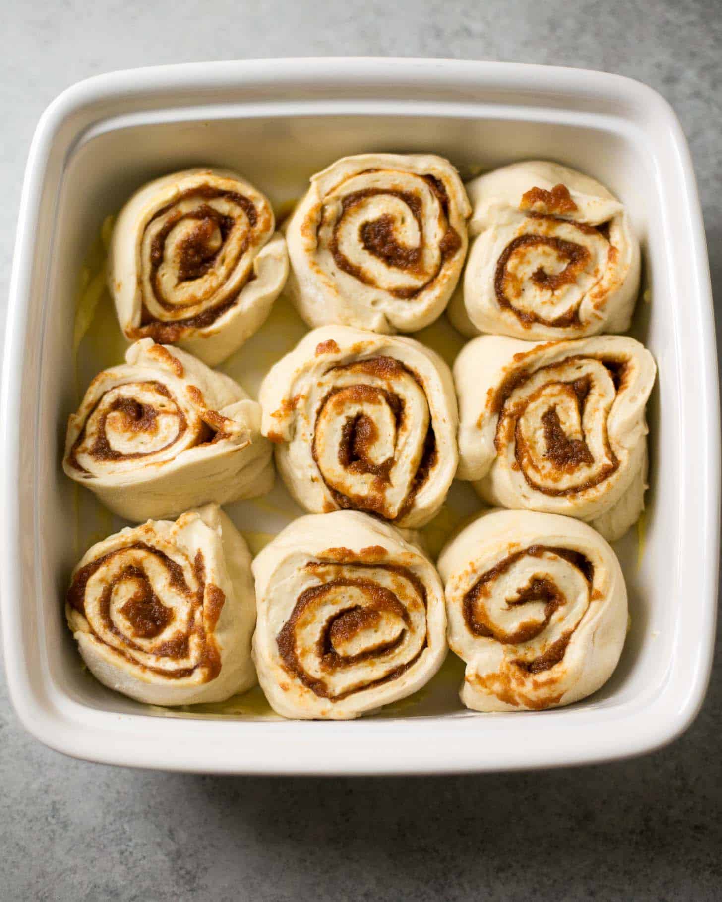 uncooked cinnamon rolls in a white baking dish