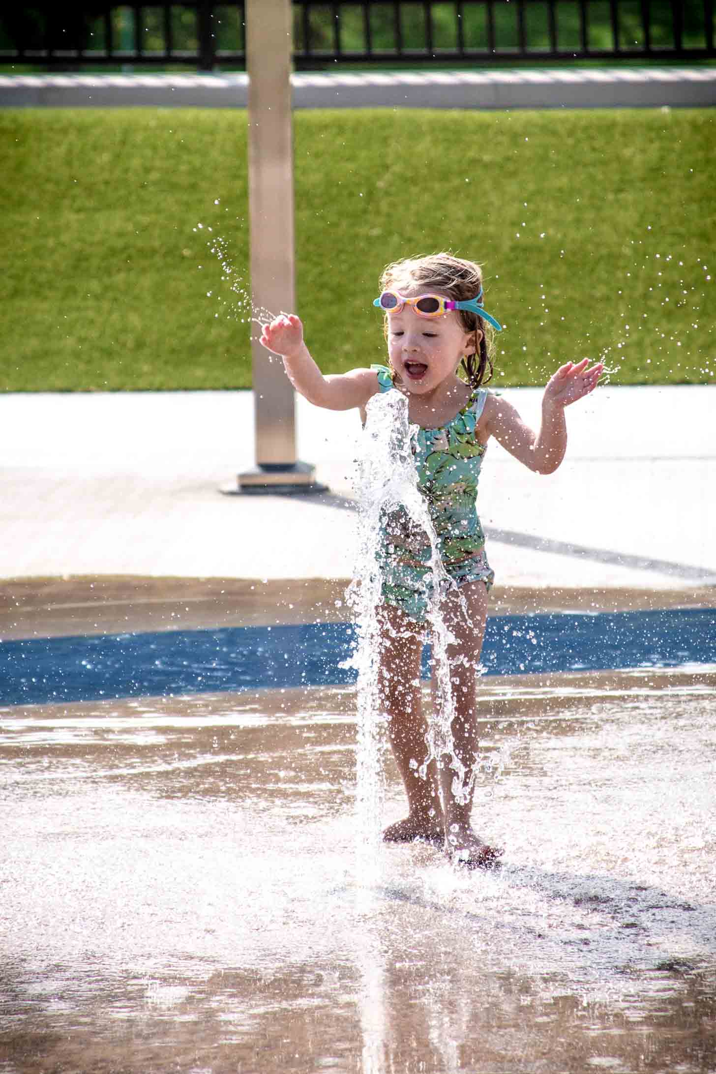 a little girl in a bathing suit and swim goggles playing in the water