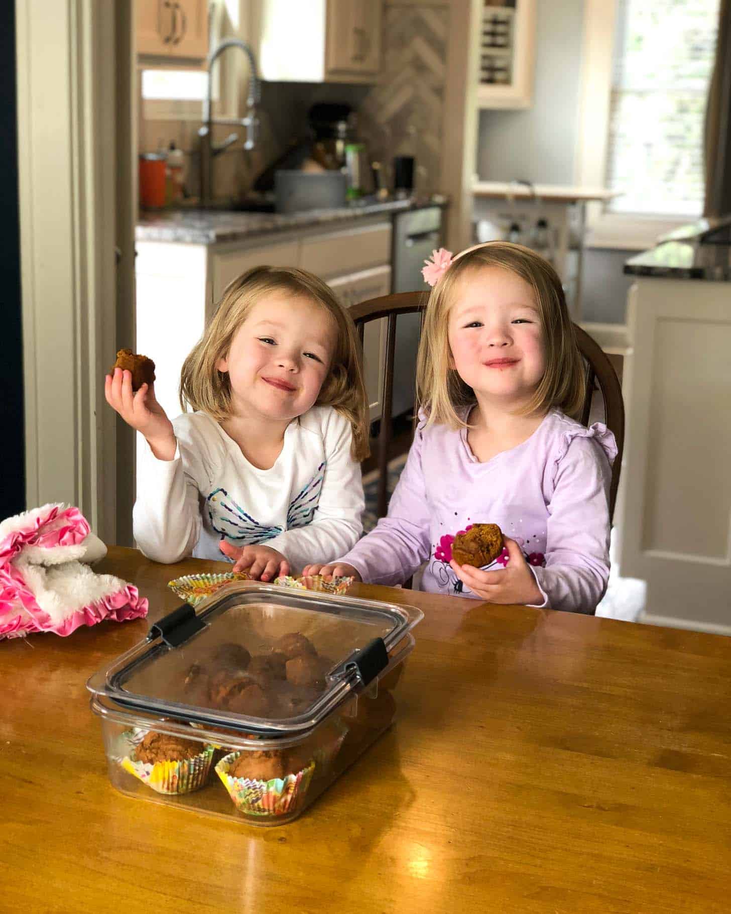 two little girls at a table eating muffins