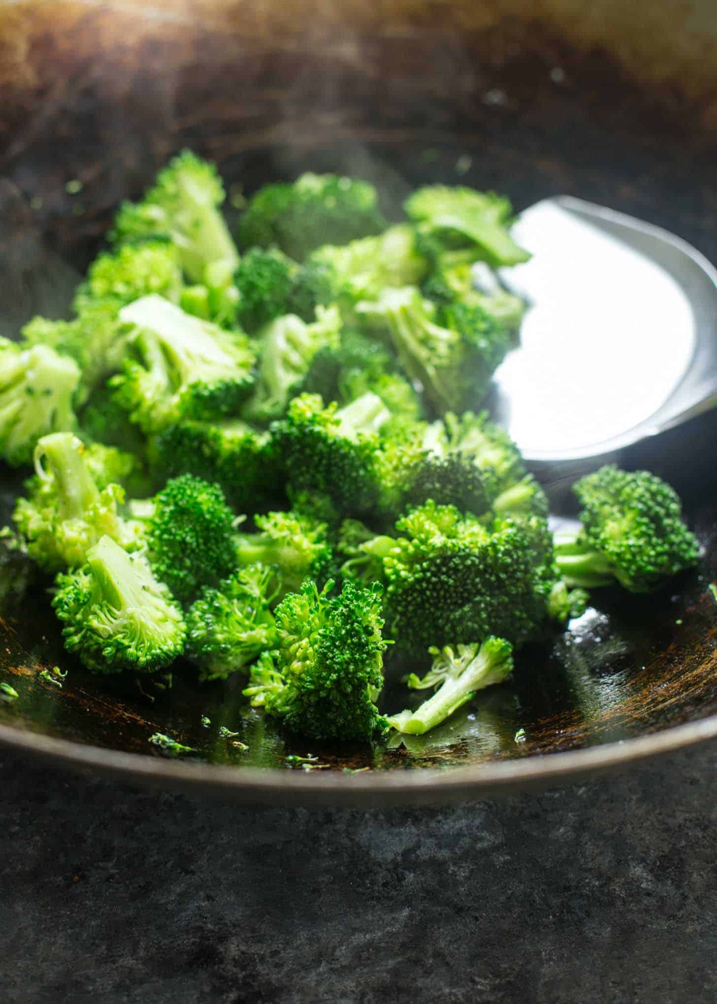 stirring broccoli florets in a wok with a spatula