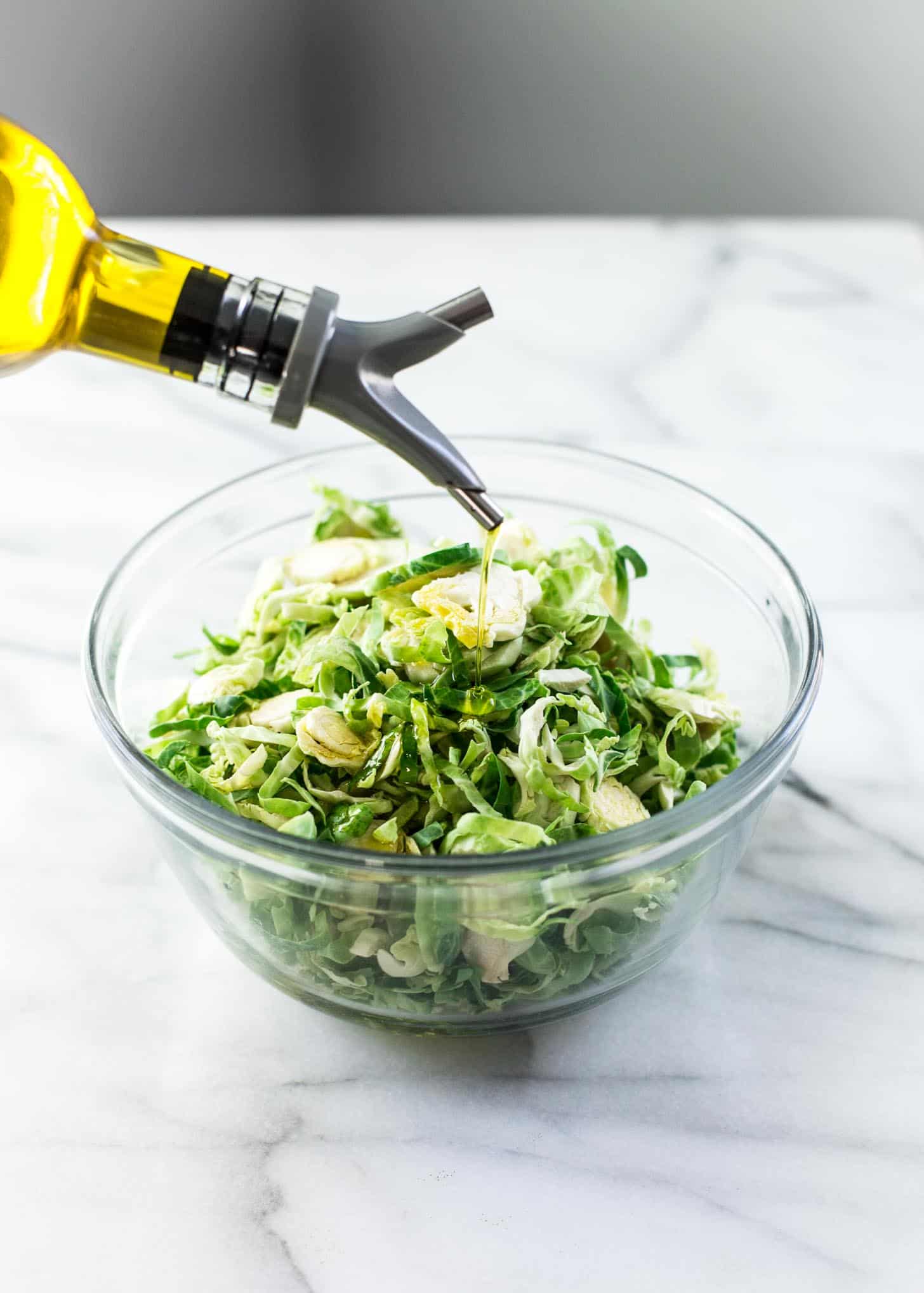 pouring oil on shredded brussels sprouts in a clear glass bowl