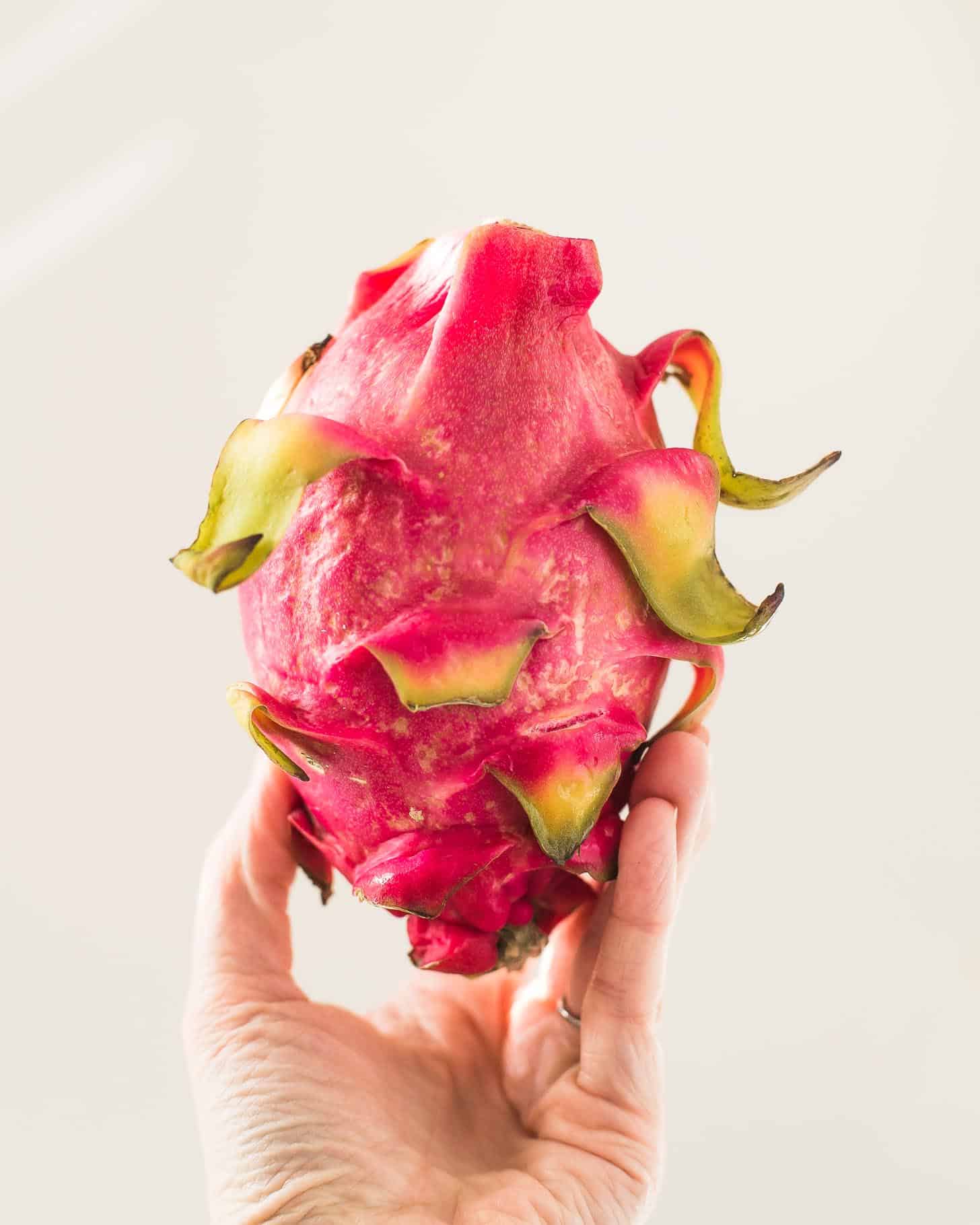 a hand holding a whole Dragon Fruit