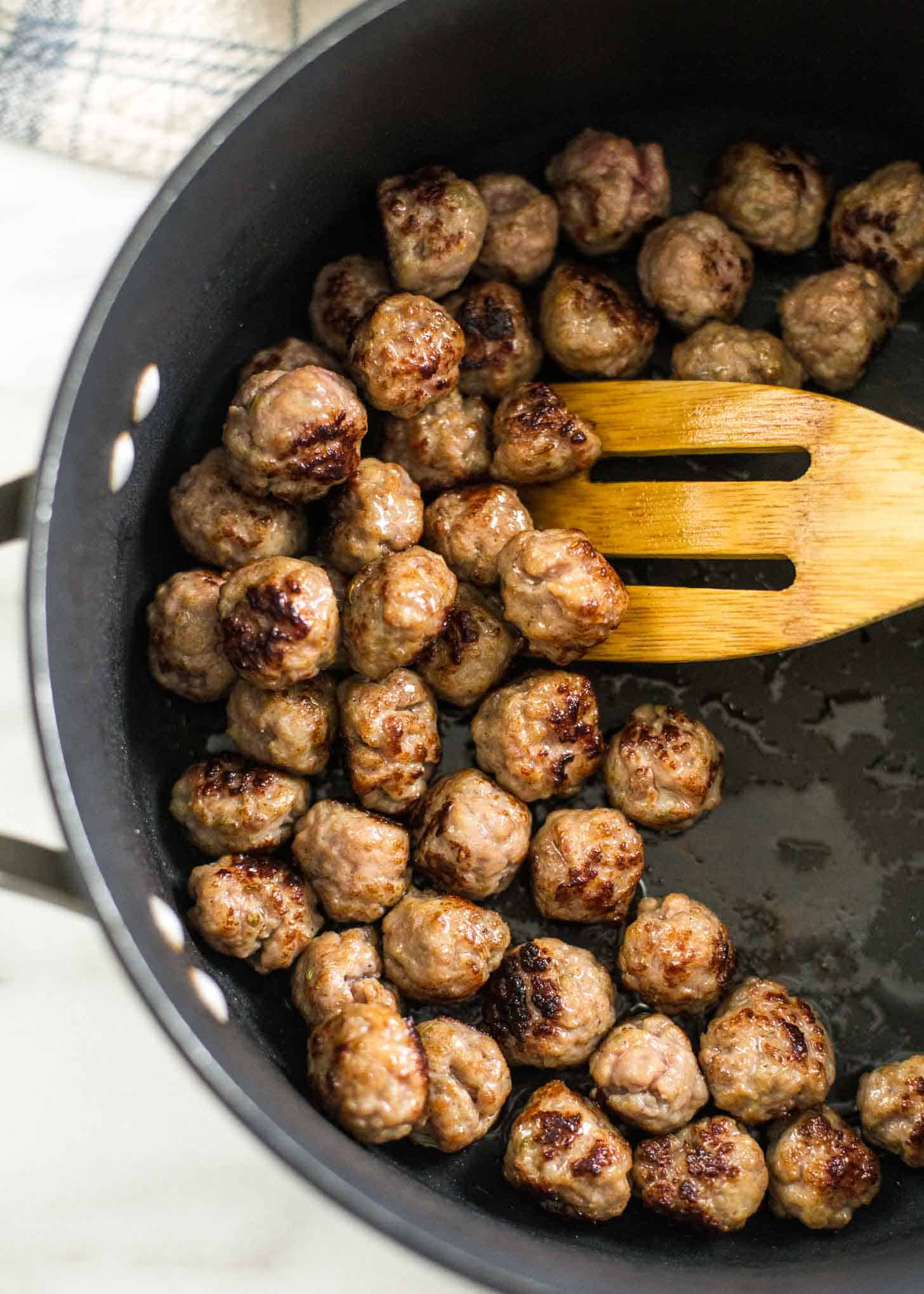 overhead image of a wooden spoon and meatballs in a large pot