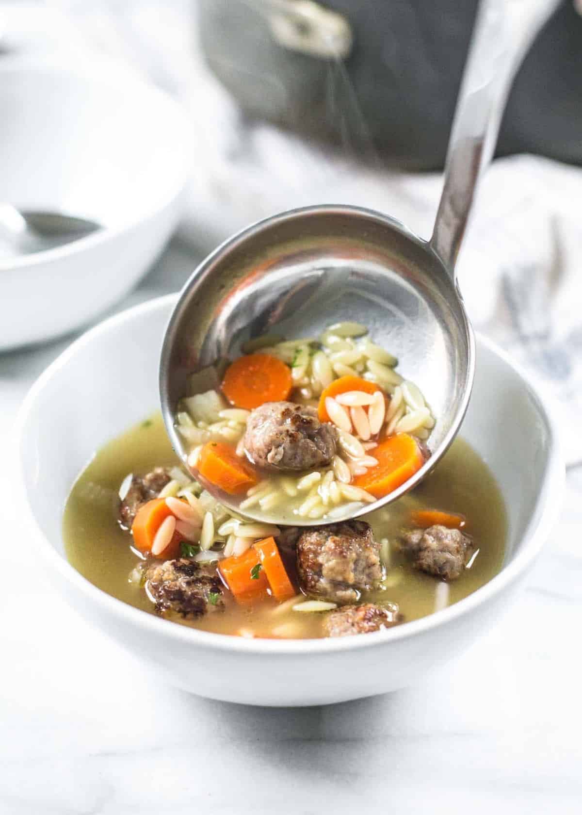 ladling Meatball and Orzo Soup into a bowl