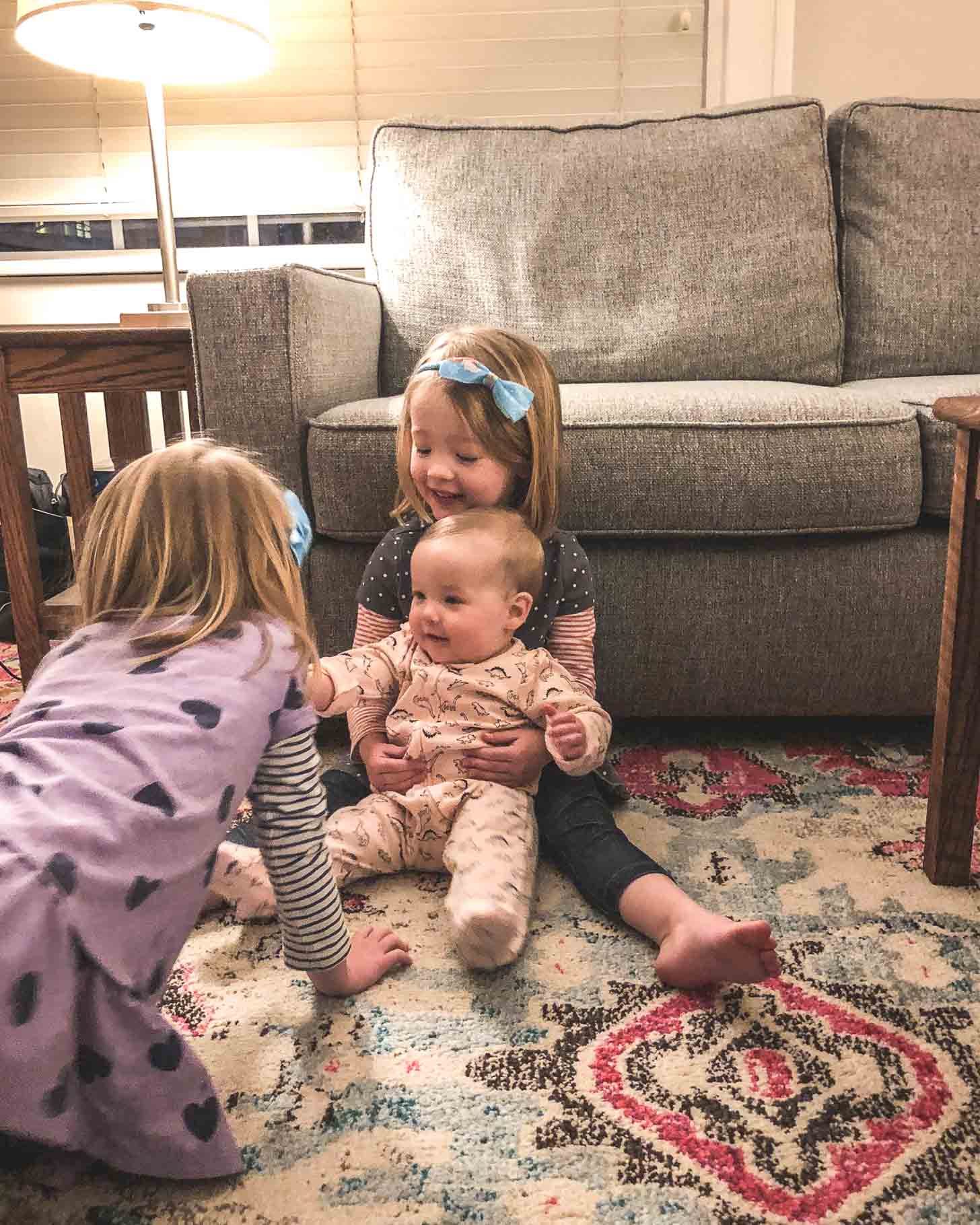 Two girls and a baby on a rug