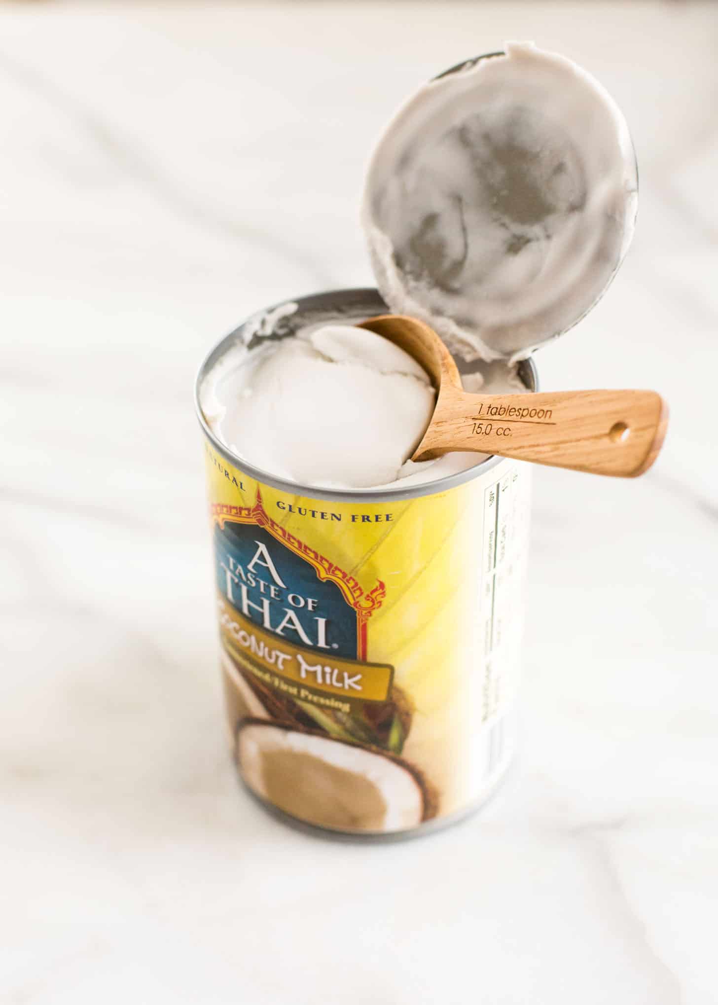 a wooden measuring spoon in a can of coconut milk