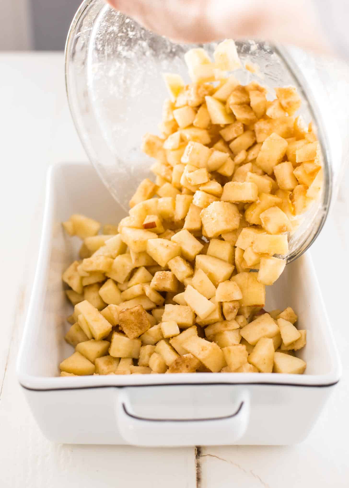 pouring seasoned apple slices into a white baking dish