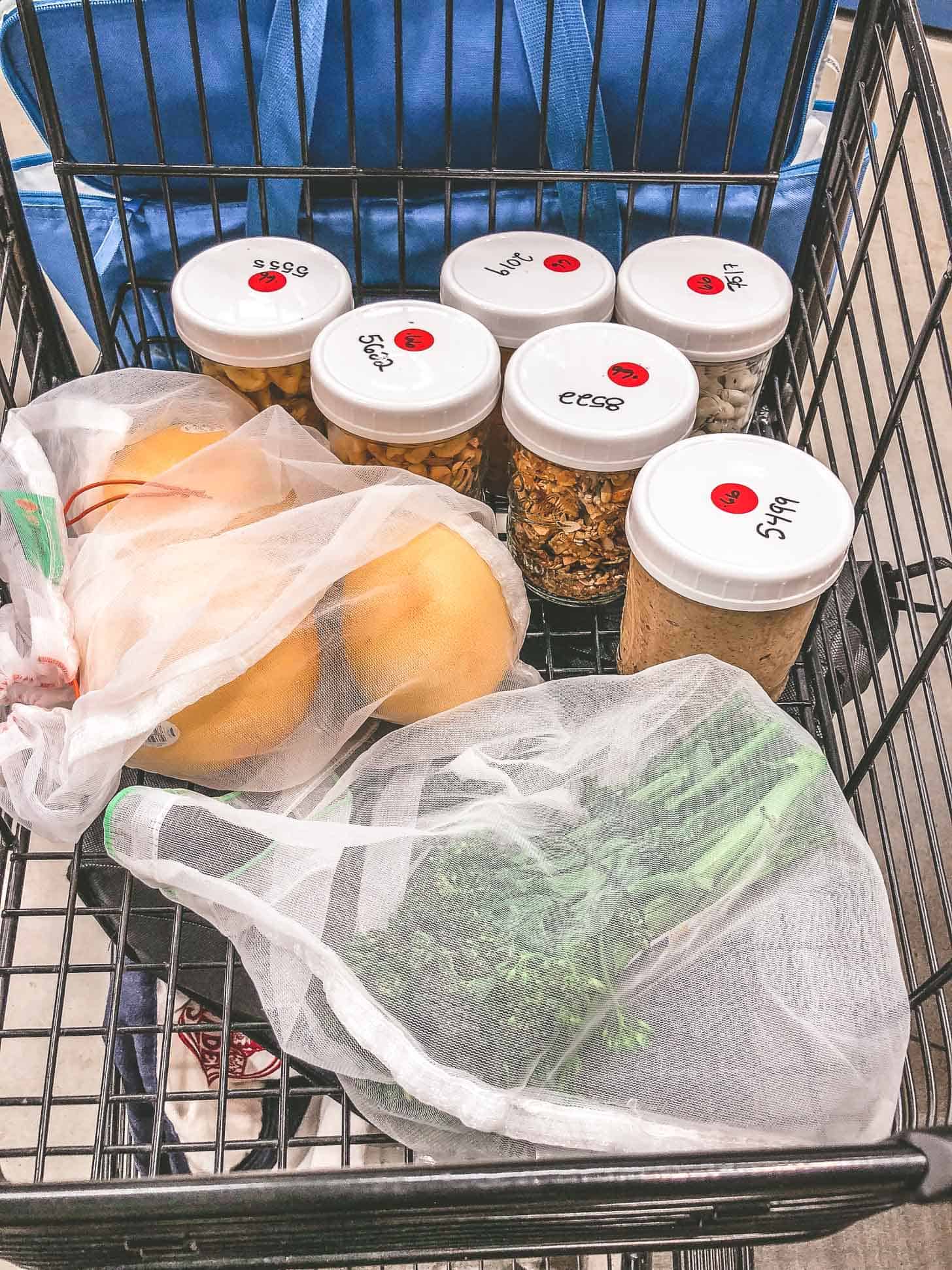 a grocery cart with mesh bags of produce and glass jars of bulk foods